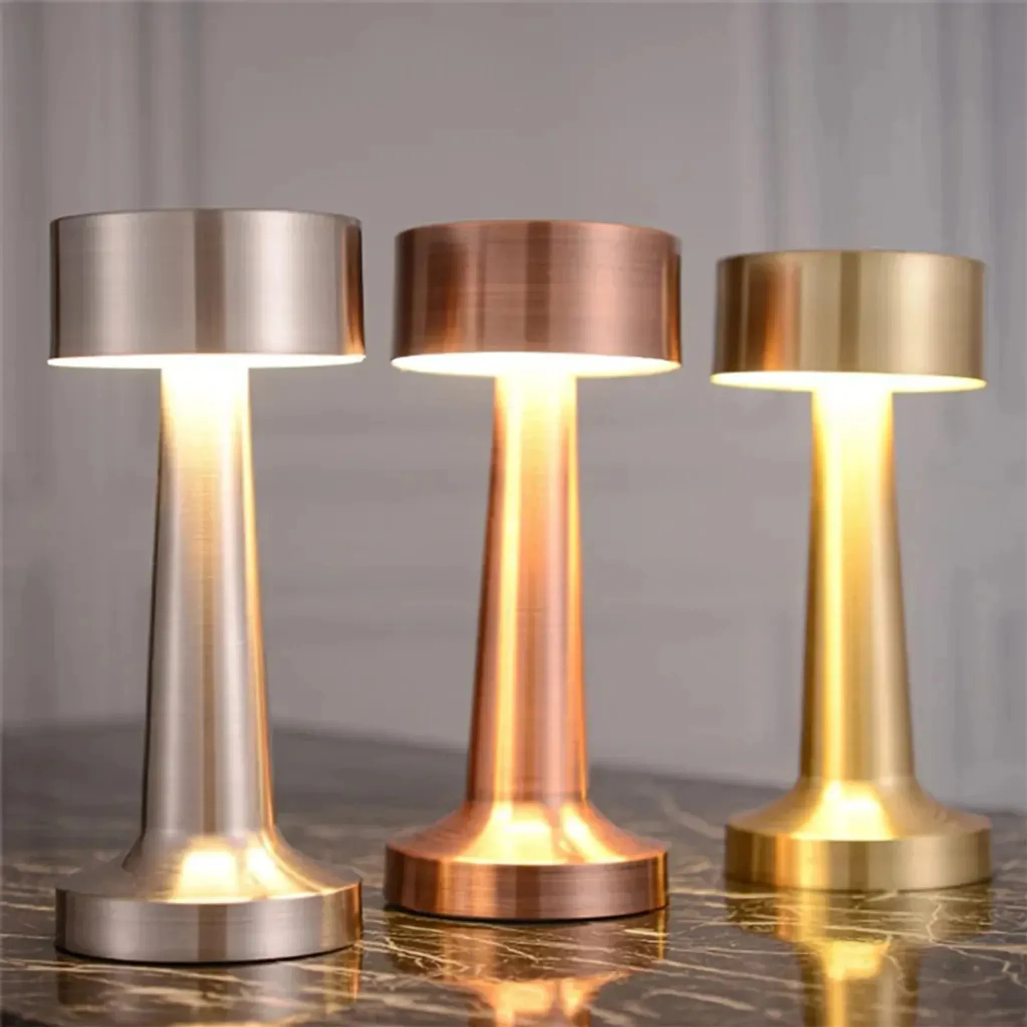 Drei metallische Lampen in verschiedenen Farben, die nach oben leuchten. Sie stehen auf einer Marmoroberfläche.