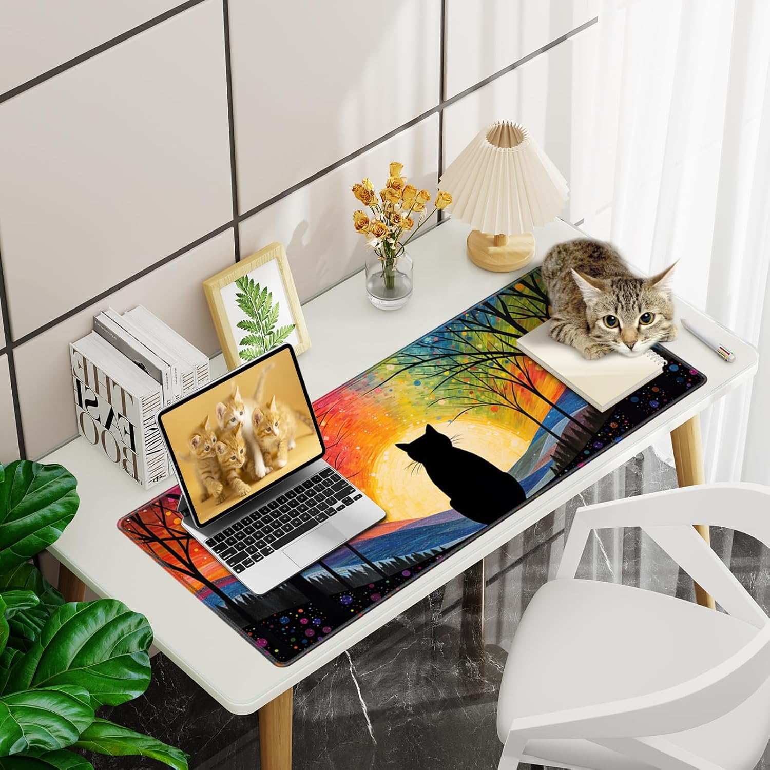 Ein Schreibtisch mit Laptop, Katze und bunter Mauspad. Eine schwarze Katzen-Silhouette ist auf dem Mousepad. Eine echte Katze liegt auf dem Schreibtisch.