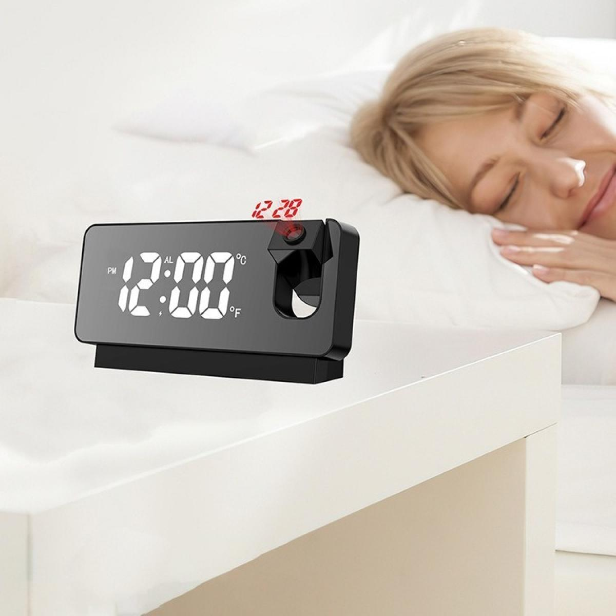 Eine Frau schläft in der Nähe einer Digitaluhr, die 12:00 PM anzeigt. Die Uhr projiziert die Zeit. Der Hintergrund zeigt ein weißes Bett.