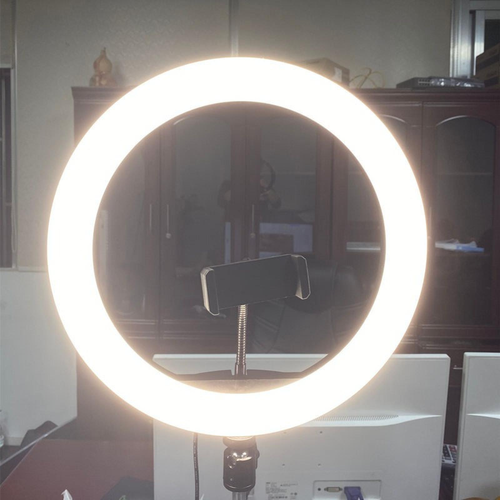 Ein Ringlicht mit Telefonhalter ist zentriert. Im Hintergrund befindet sich ein brauner Schrank. Unten befindet sich ein Computermonitor.