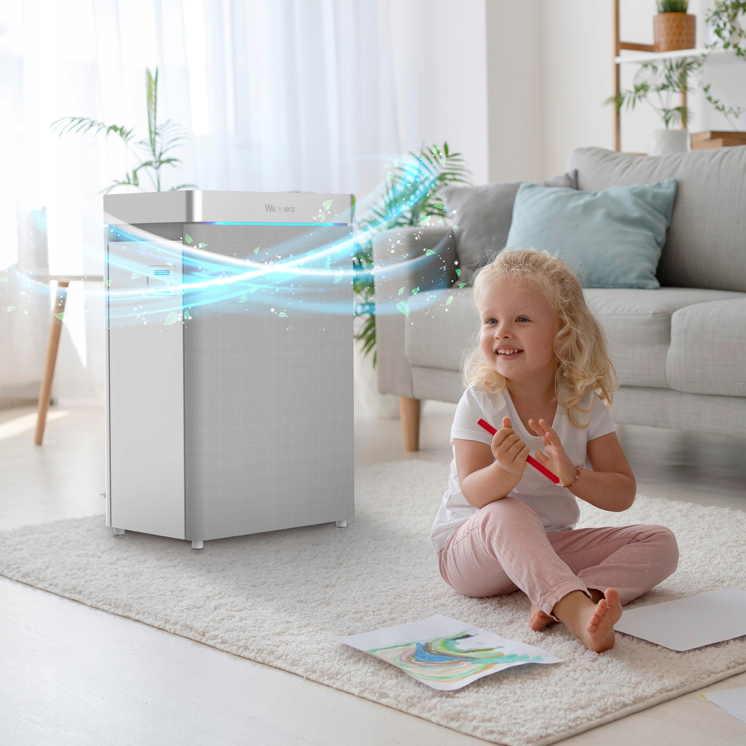 Dziewczynka siedzi na dywanie z rysunkami. Obok niej oczyszczacz powietrza. Scena ma miejsce w jasnym salonie.