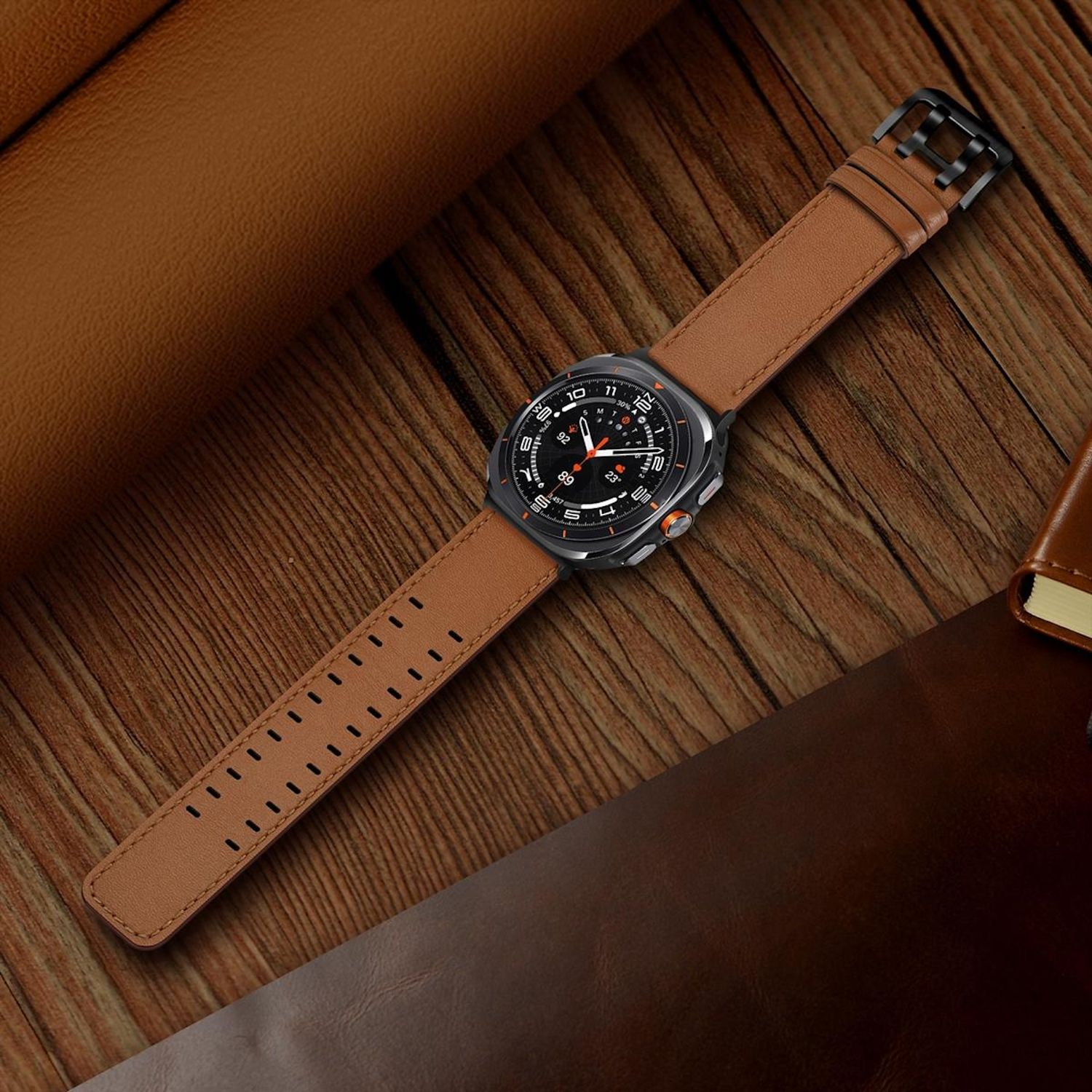 Eine braune Lederuhr auf einer Holzoberfläche. Die Uhr ist schwarz mit orangefarbenen Akzenten. Ein Leder-Notizbuch im Hintergrund.