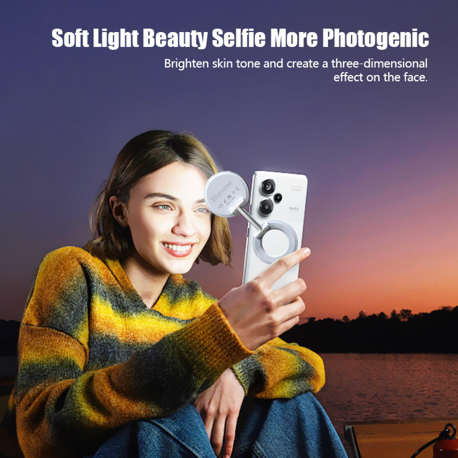 Eine Frau macht ein Selfie mit einem Telefon und einem Ringlicht. Sie trägt einen Pullover, mit einem See und Sonnenuntergang im Hintergrund.