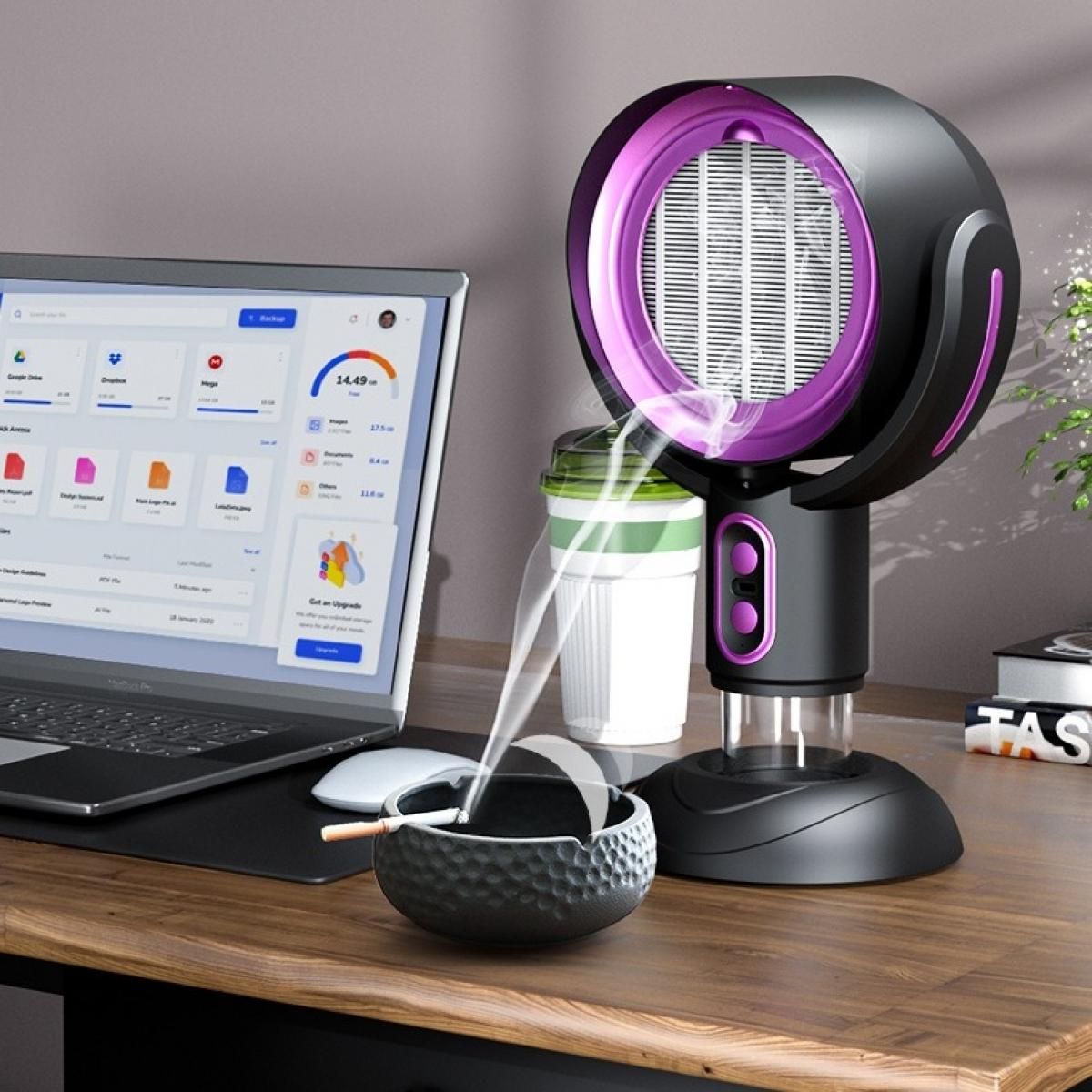 Ein Schreibtisch mit Laptop, Ventilator, Becher und Aschenbecher mit brennender Zigarette, die Rauch abgibt.