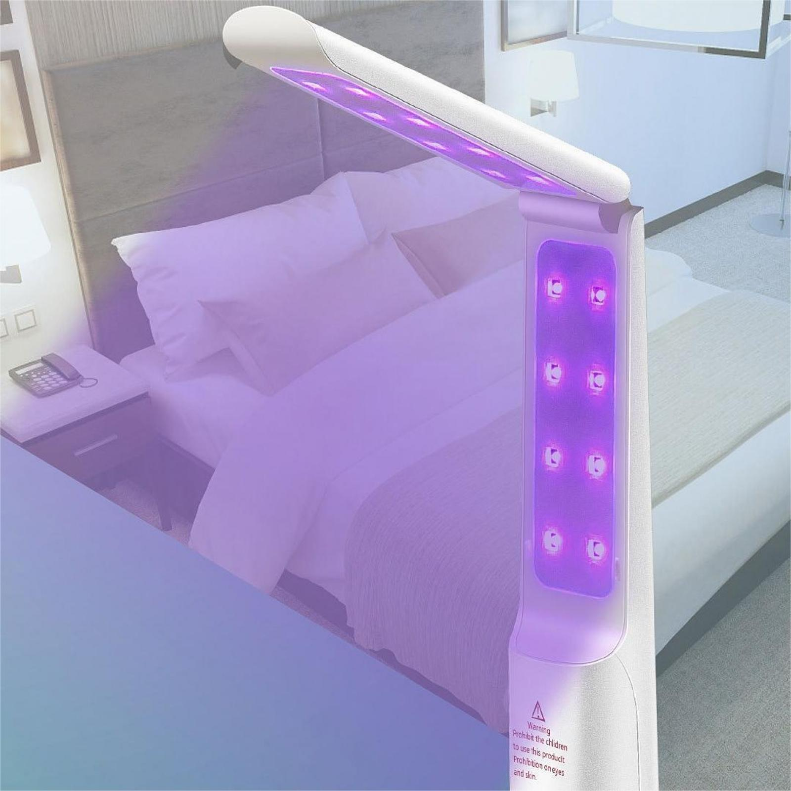 Ein weißes UV-Lichtgerät, das lila leuchtet, steht neben einem Bett mit weißer Bettwäsche. Warnhinweis sichtbar.