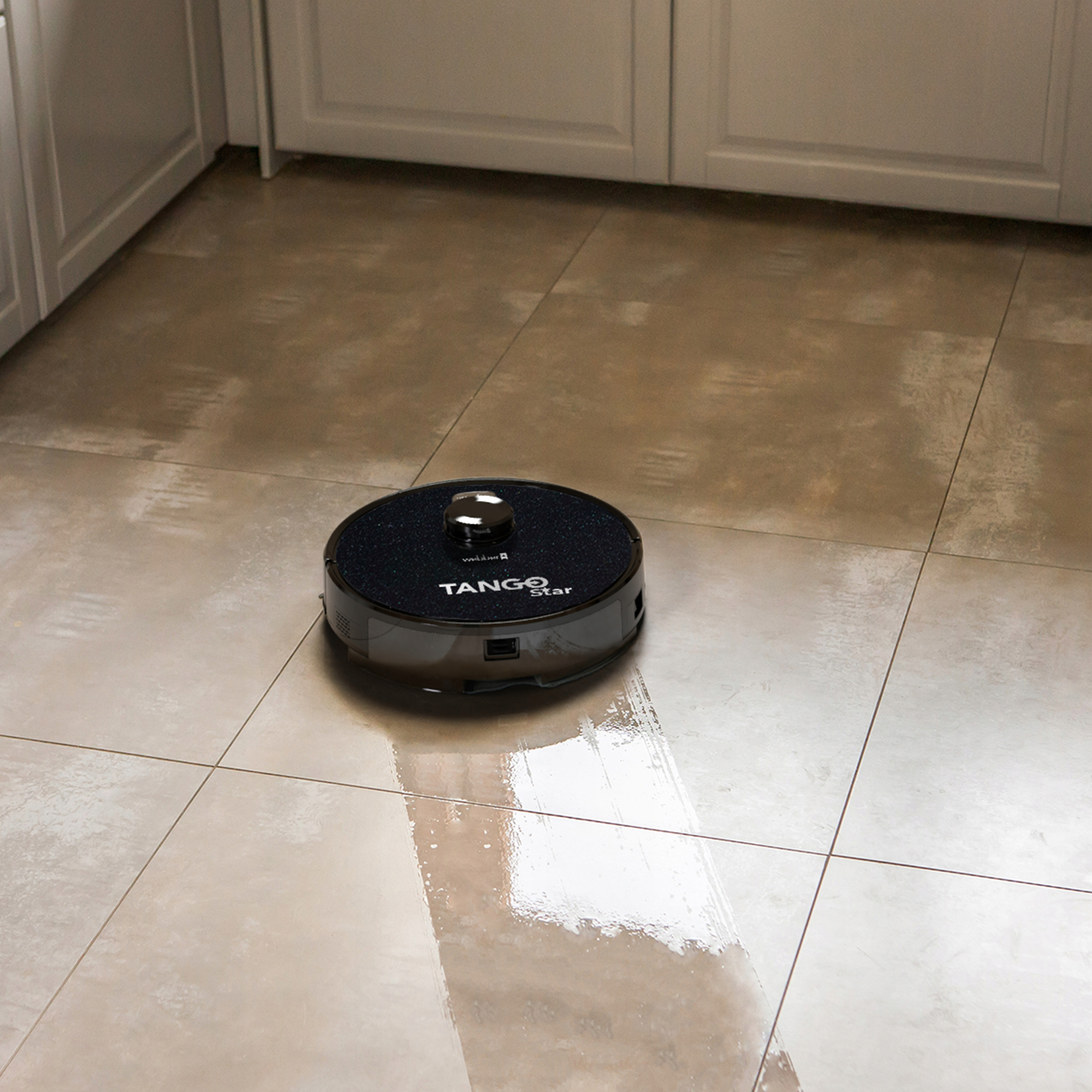 Robot sprzątający Tango Star czyści beżową podłogę. Białe szafki w tle.