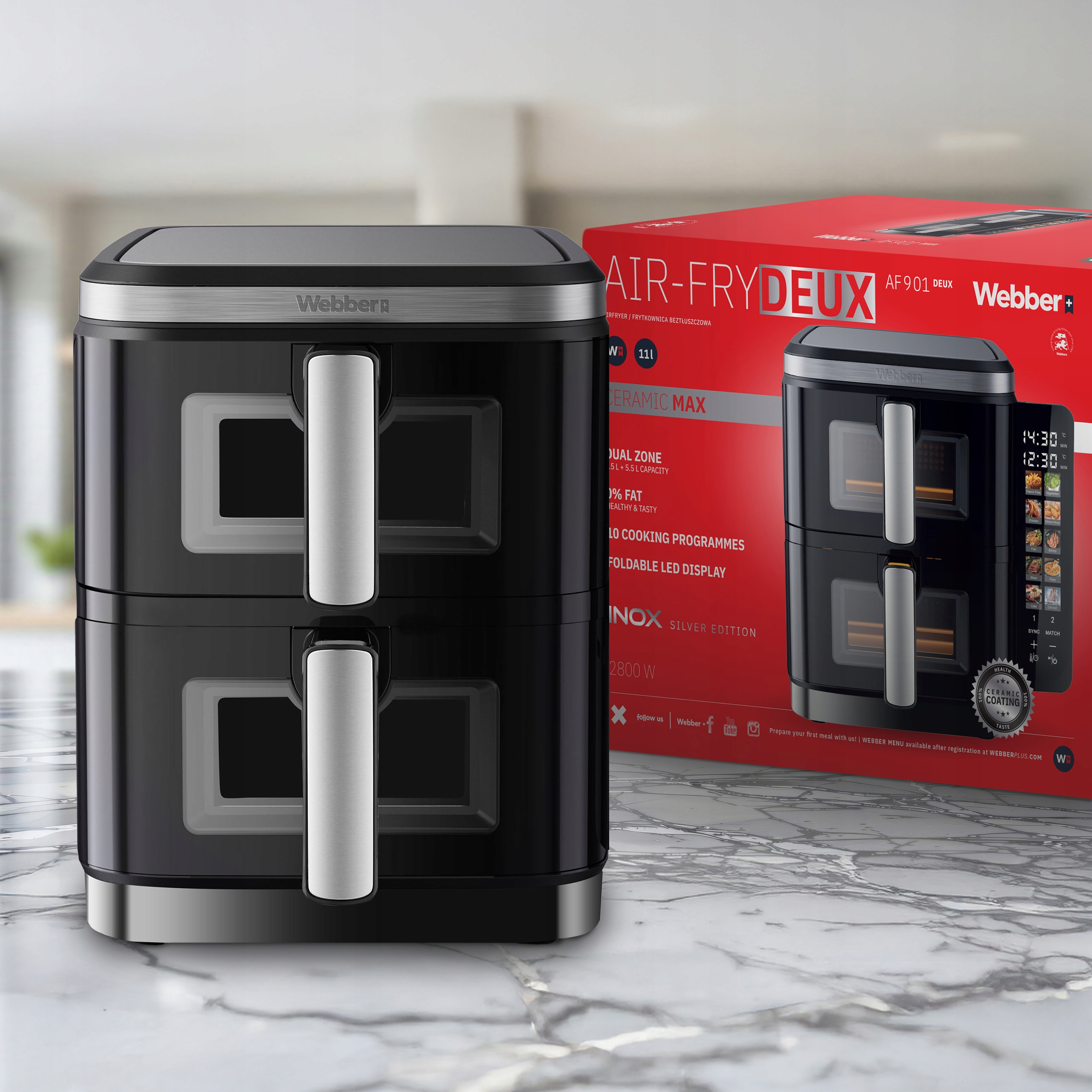 Czarna frytkownica powietrzna ze srebrnymi akcentami i czerwonym pudełkiem na marmurowej powierzchni. Pudełko pokazuje obraz.