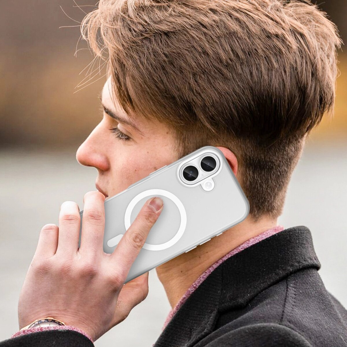 Ein Mann hält ein Telefon an sein Ohr. Das Telefon hat eine Hülle mit einem weißen Kreis. Er trägt einen schwarzen Mantel und eine Uhr.