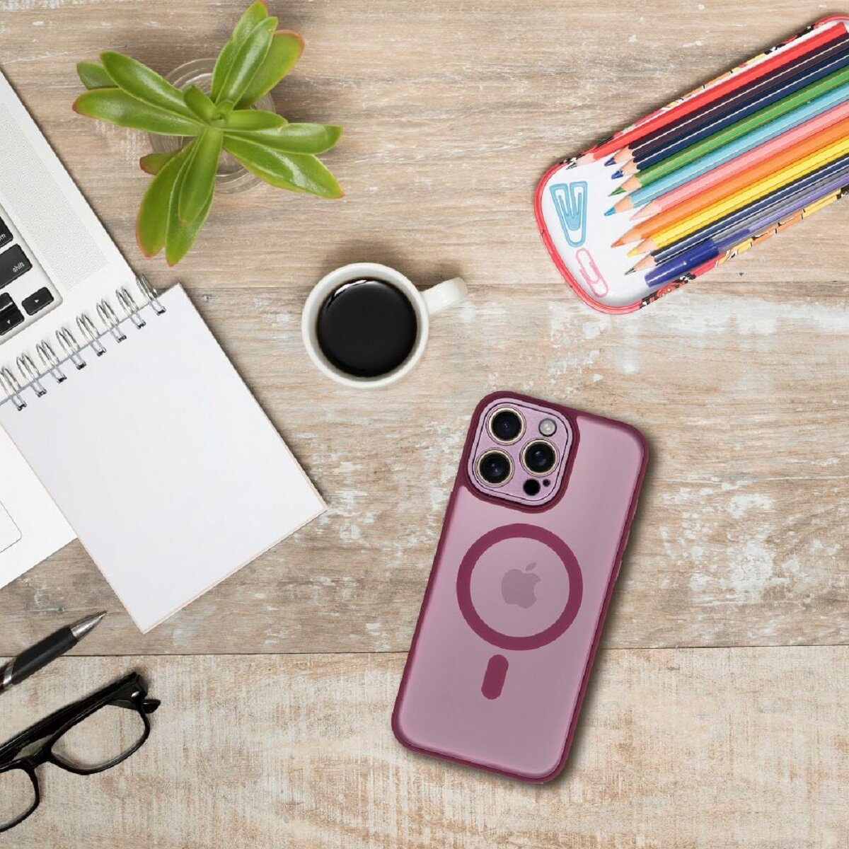 Ein Schreibtisch mit Handyhülle, Bleistiften, Kaffee, Notizblock, Brille und einer Sukkulente. Die Handyhülle ist lila. Der Hintergrund ist ein Holzschreibtisch.