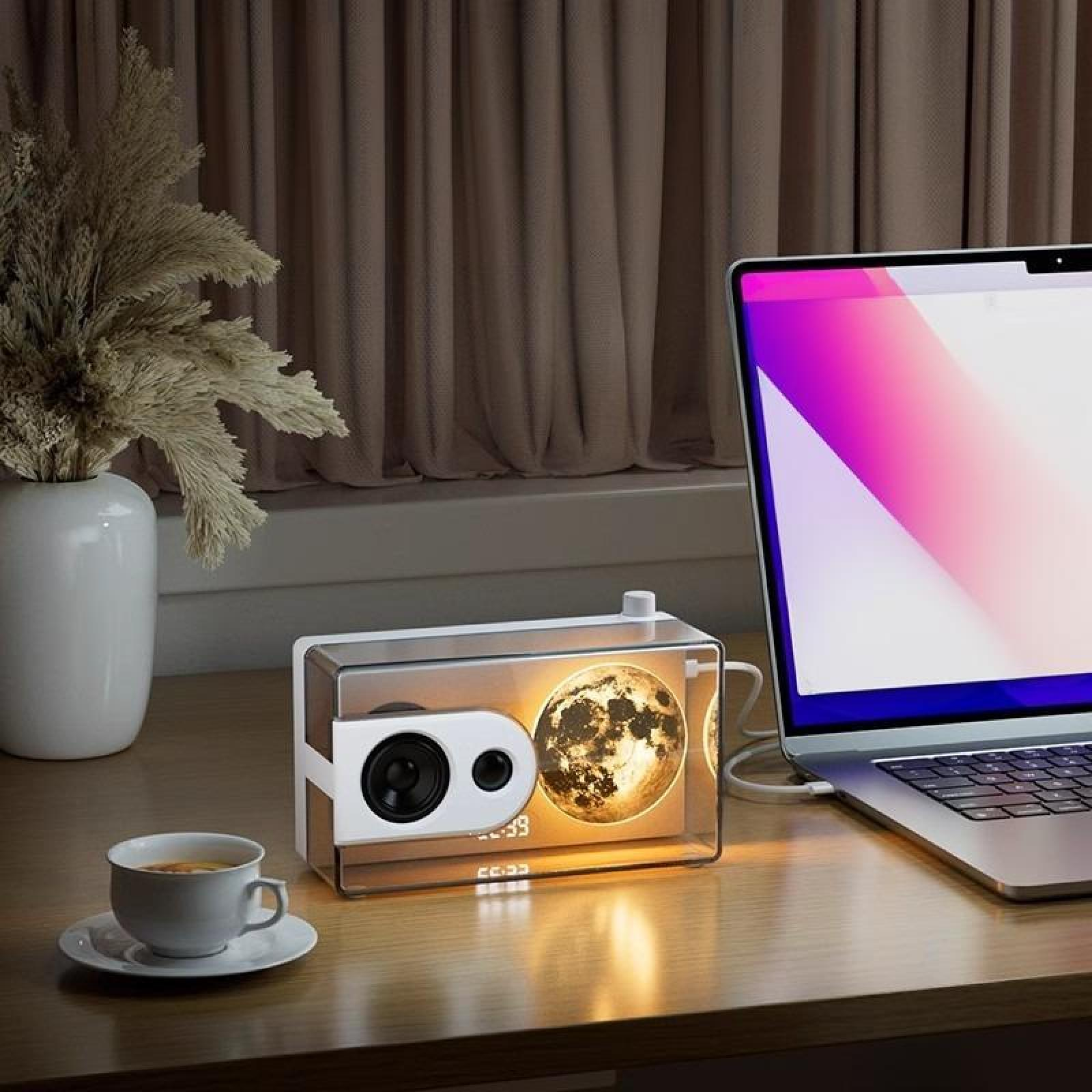 Eine Schreibtischszene mit Lautsprecher, Laptop, Kaffeetasse und einer Vase mit Pflanzen. Der Lautsprecher zeigt ein Mondbild.
