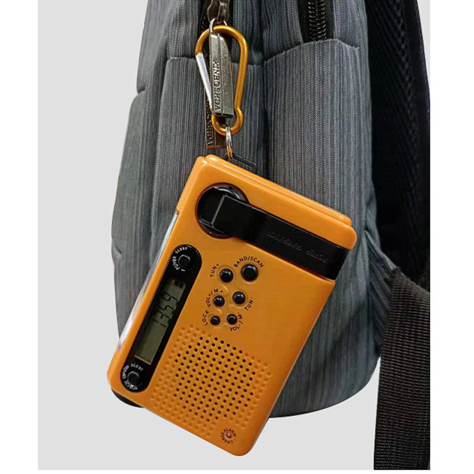 Ein orangefarbenes Radio hängt an einem Rucksack. Es zeigt 13:59 an. Das Radio ist mit einem goldenen Karabiner befestigt.