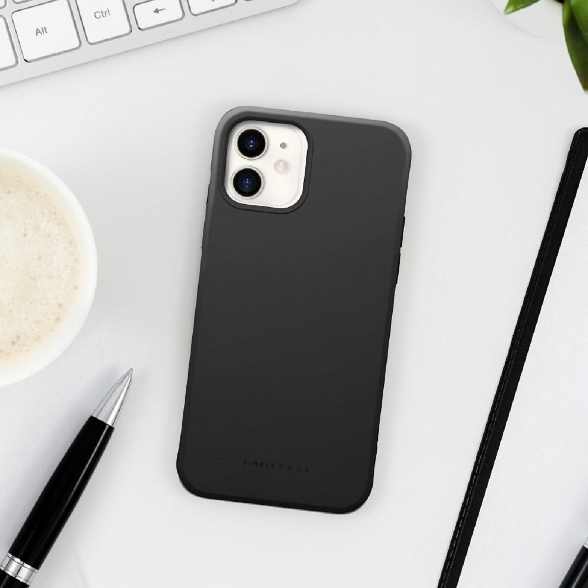 Schwarzes iPhone in einer Hülle auf einem weißen Schreibtisch. Eine Kaffeetasse, ein Stift, eine Tastatur und ein Notizbuch sind ebenfalls vorhanden.