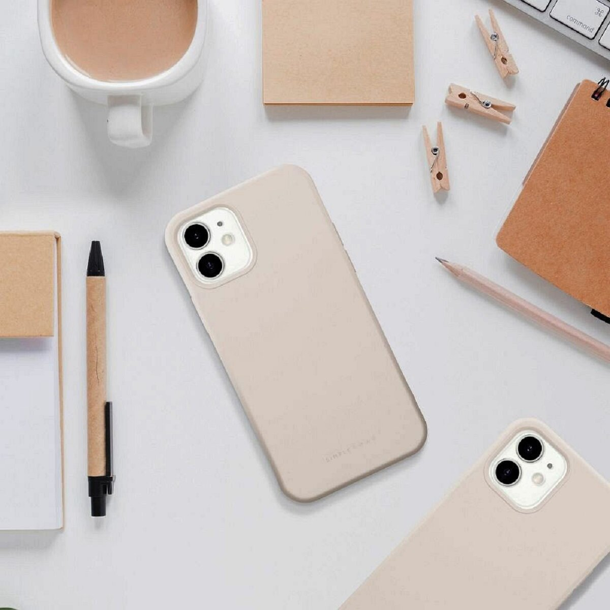Eine beige Handyhülle und eine weitere liegen auf einer weißen Oberfläche mit einer Kaffeetasse, einem Stift und einem Notizblock.