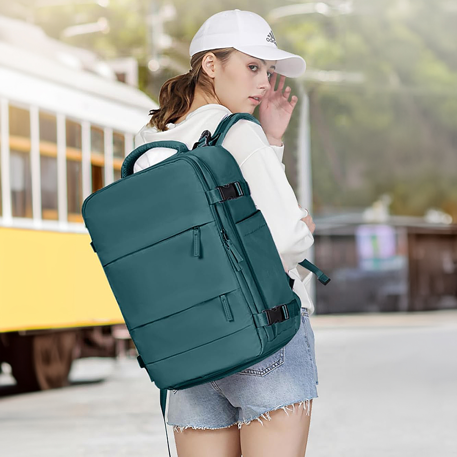 Una donna con un berretto bianco e uno zaino verde acqua guarda sopra la spalla. Un treno giallo sullo sfondo.