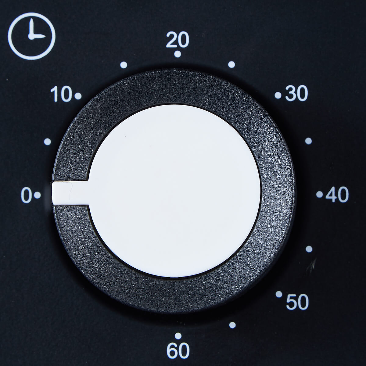 Zbliżenie czarnej tarczy timera piekarnika z białymi cyframi i białym środkiem. Pokrętło jest ustawione blisko zera.