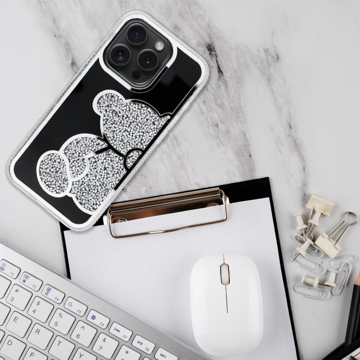 Ein Telefoncase mit Kristallbär, Tastatur, Maus, Klemmbrett und Büroartikel auf Marmoroberfläche.