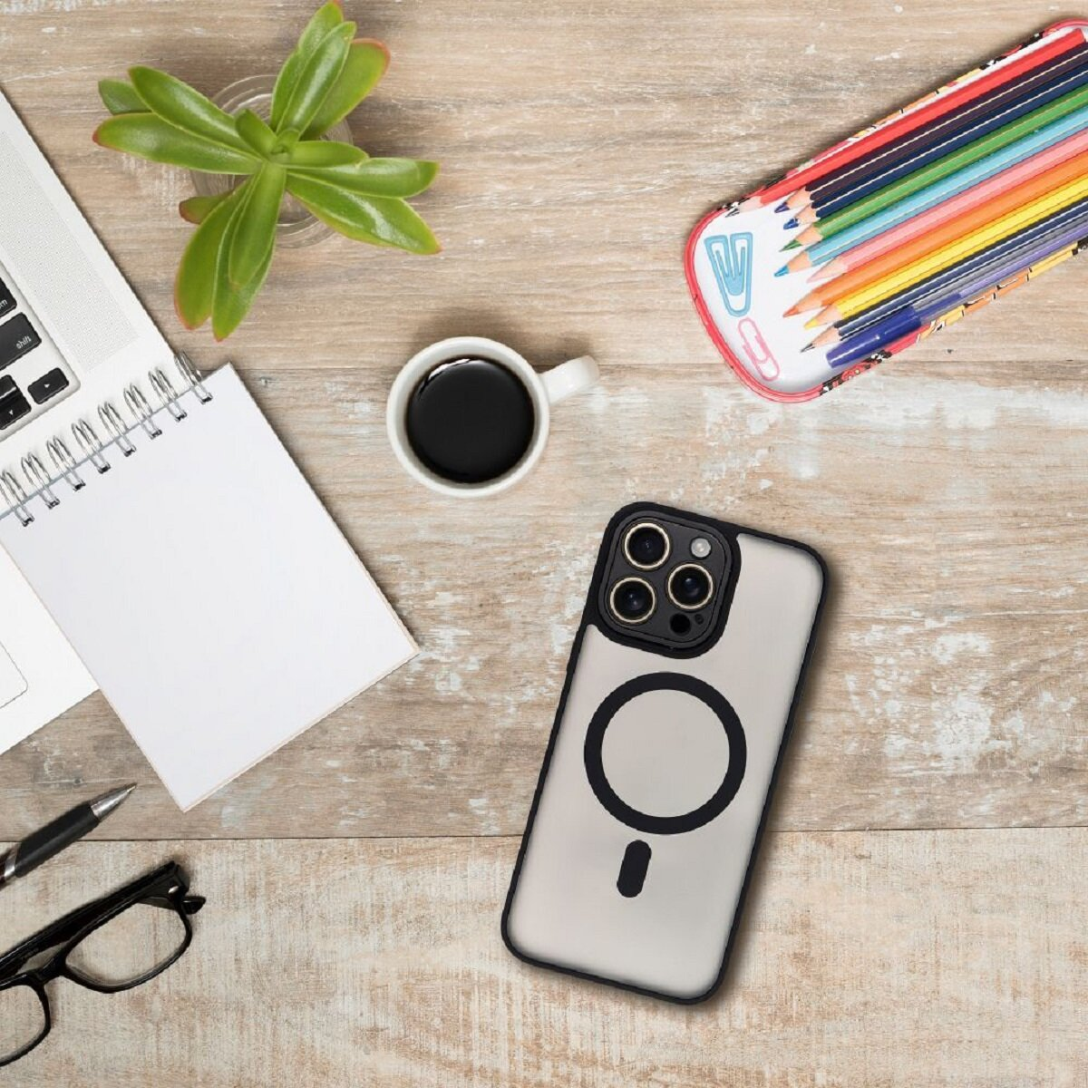 Schreibtisch mit Laptop, Notizblock, Kaffee, Telefon, Bleistiften, Pflanze und Brille. Gegenstände liegen auf Holz.