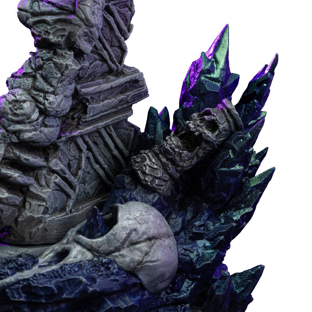 Primo piano di una scultura fantasy con teschi, cristalli e strutture in pietra. Colori: grigio, viola e nero su sfondo bianco.