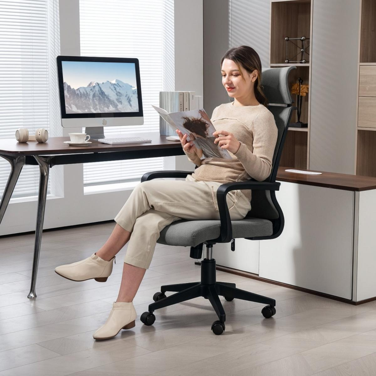 Eine Frau liest eine Zeitschrift, während sie in einem Bürostuhl sitzt. Ein Schreibtisch mit Computer und Bücherregal im Hintergrund.