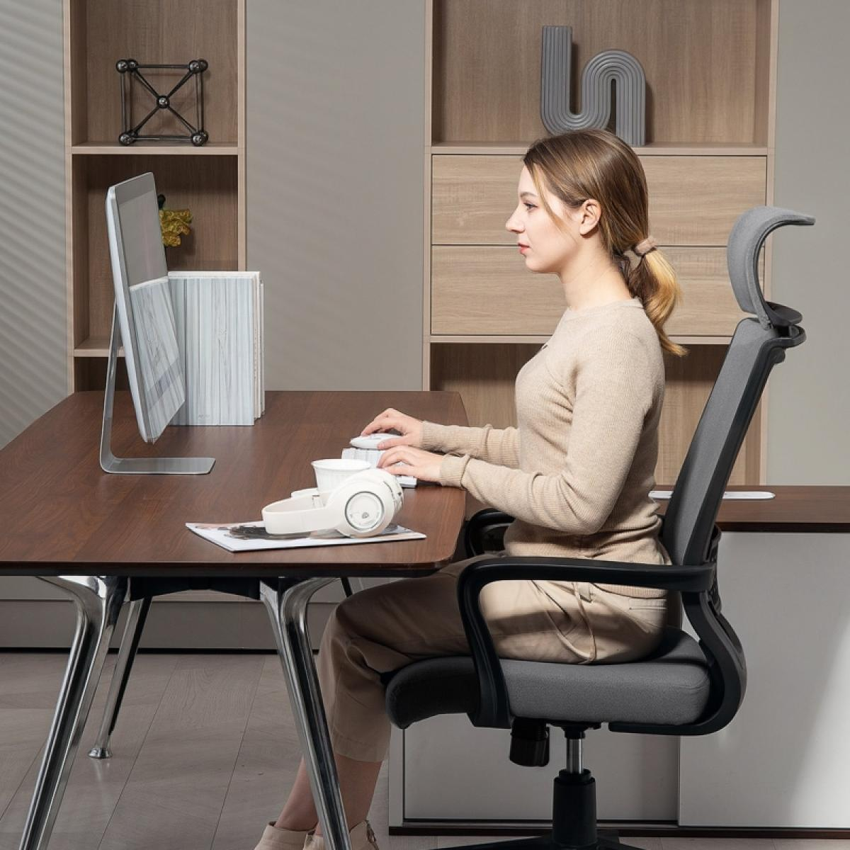Eine Frau sitzt an einem Schreibtisch und tippt auf einer Tastatur. Ein Computermonitor, Kopfhörer und Dekorationsartikel befinden sich auf dem Schreibtisch.