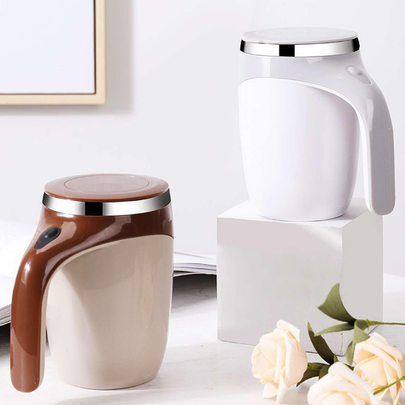Zwei elektrische Becher, einer braun und einer weiß, mit silbernen Rändern. Weißer Becher auf einem weißen Block. Rosen im Vordergrund.