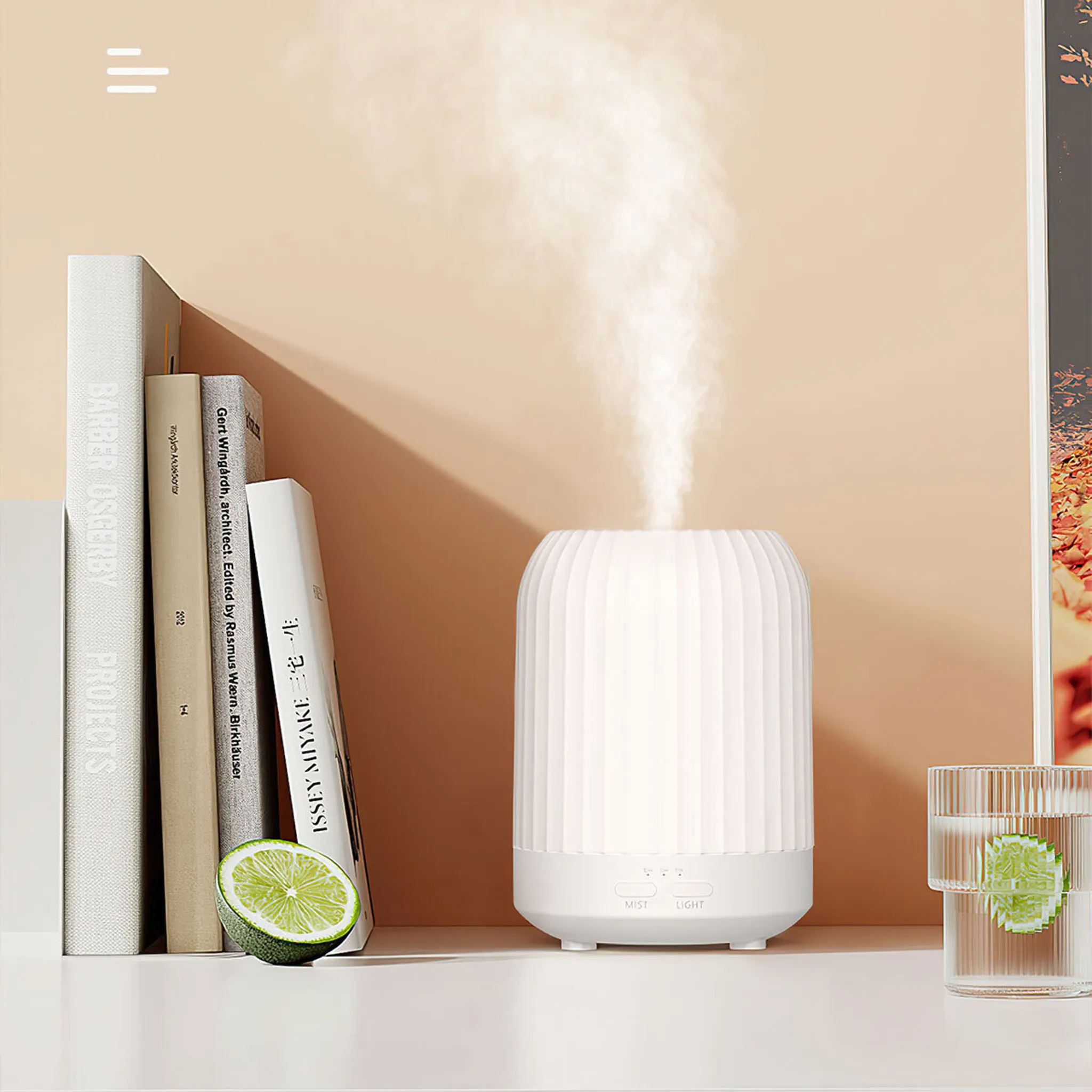 Ein weißer Diffusor gibt Dampf ab. Bücher, eine Limette und ein Wasserglas sind in der Nähe. Der Hintergrund ist warmbeige.