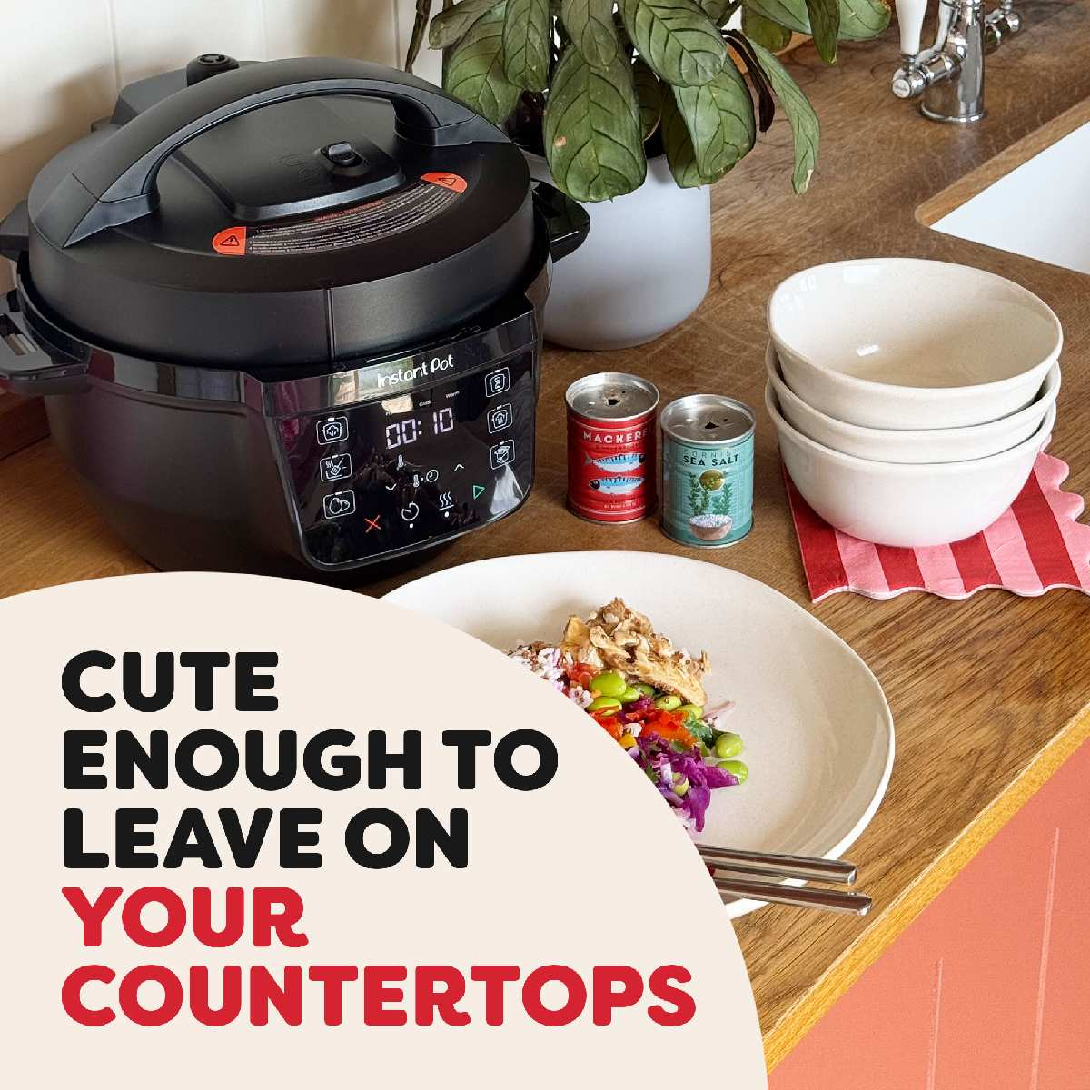 Czarny Instant Pot obok jedzenia na talerzu, małych puszek i misek. Rośliny i tekst 'CUTE ENOUGH TO LEAVE ON YOUR COUNTERTOPS'.