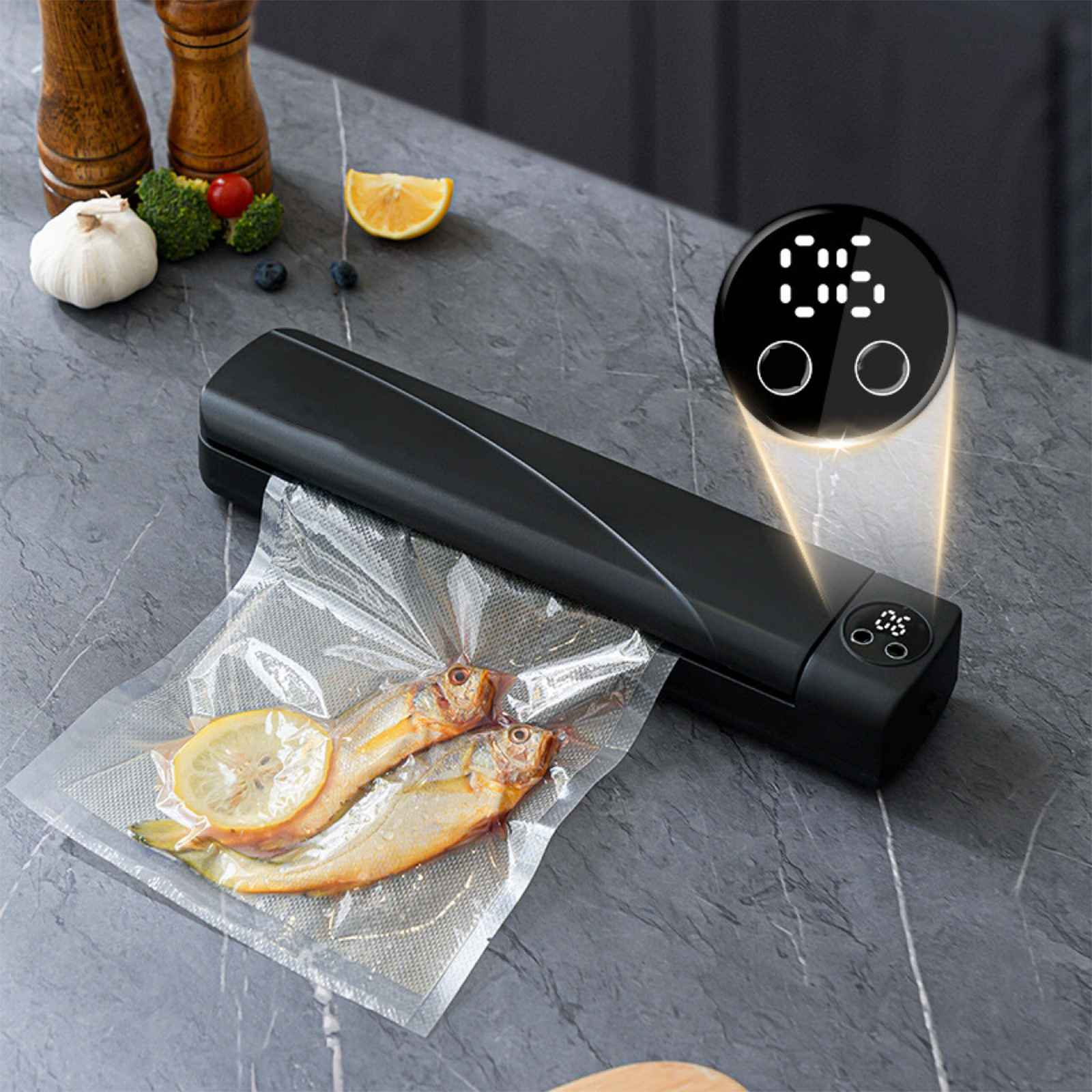 Ein schwarzes Vakuumiergerät mit Fisch in einer Tüte. Zitronenscheibe und Gemüse liegen auf dem Tisch. Ein digitales Display ist sichtbar.