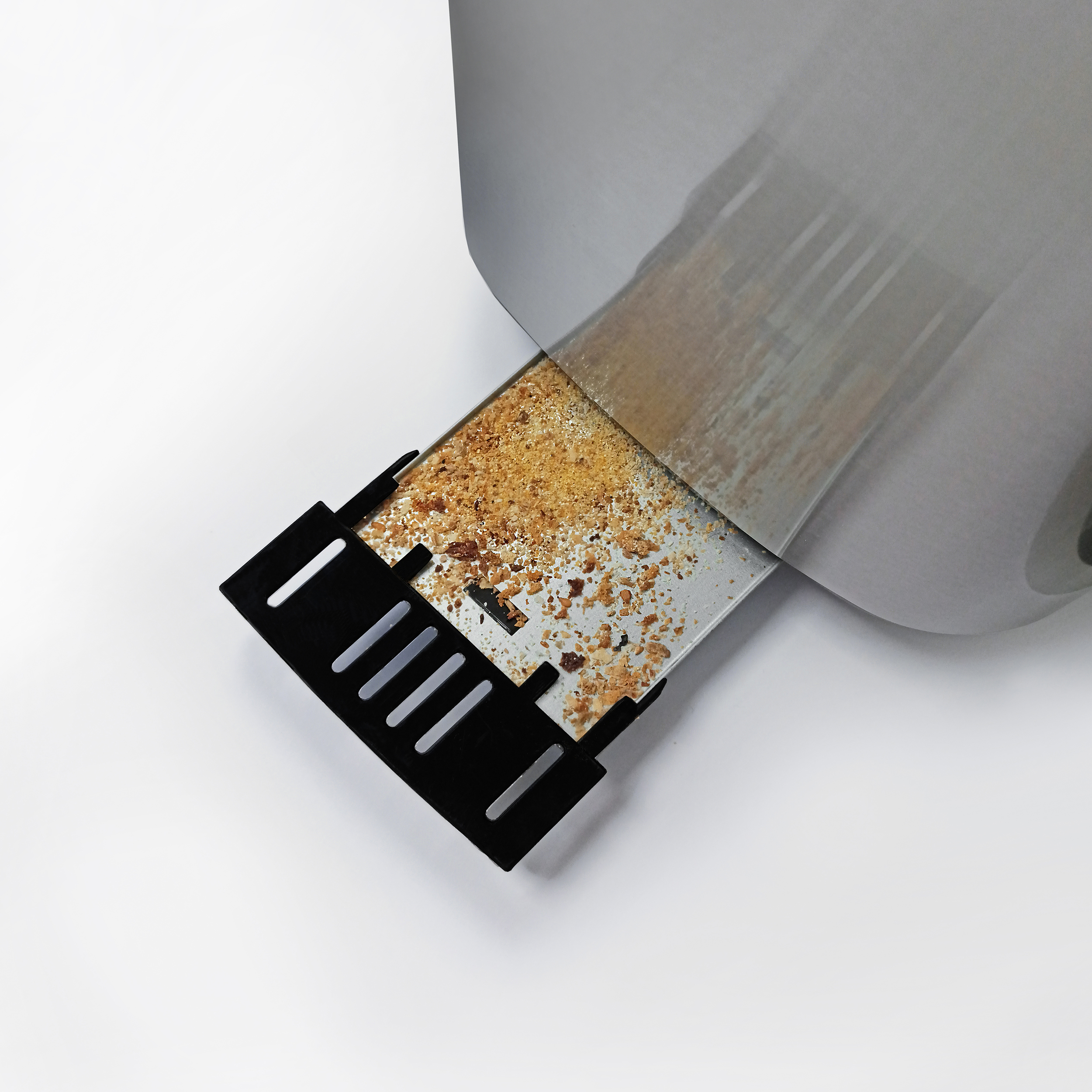 Ein Metalltablett mit Krümeln ist teilweise von einem grauen Blatt bedeckt. Unten befindet sich ein schwarzes Plastikteil.