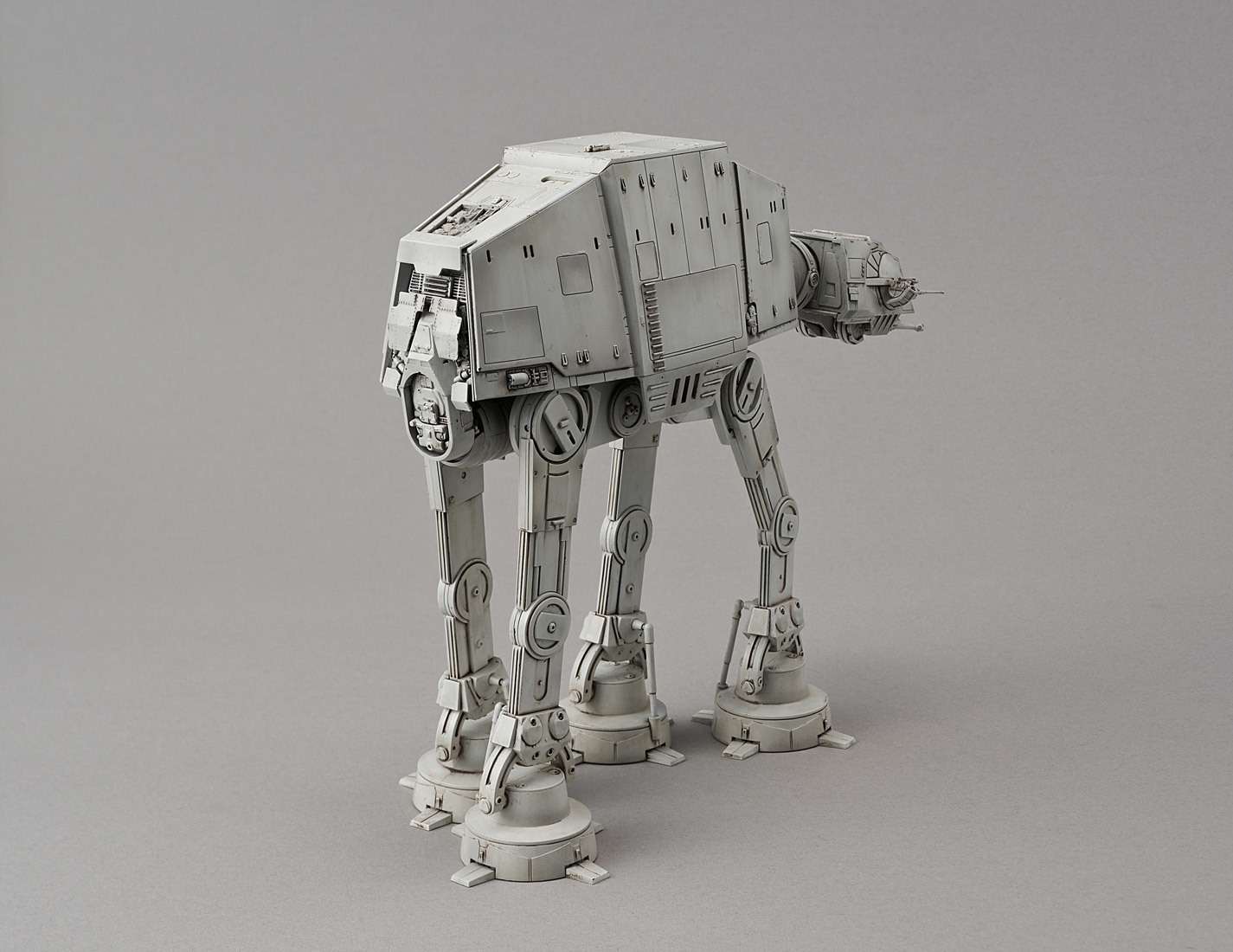 Un modèle gris d'AT-AT de Star Wars. Il repose sur quatre pattes, avec un corps rectangulaire et une tourelle. Fond gris.