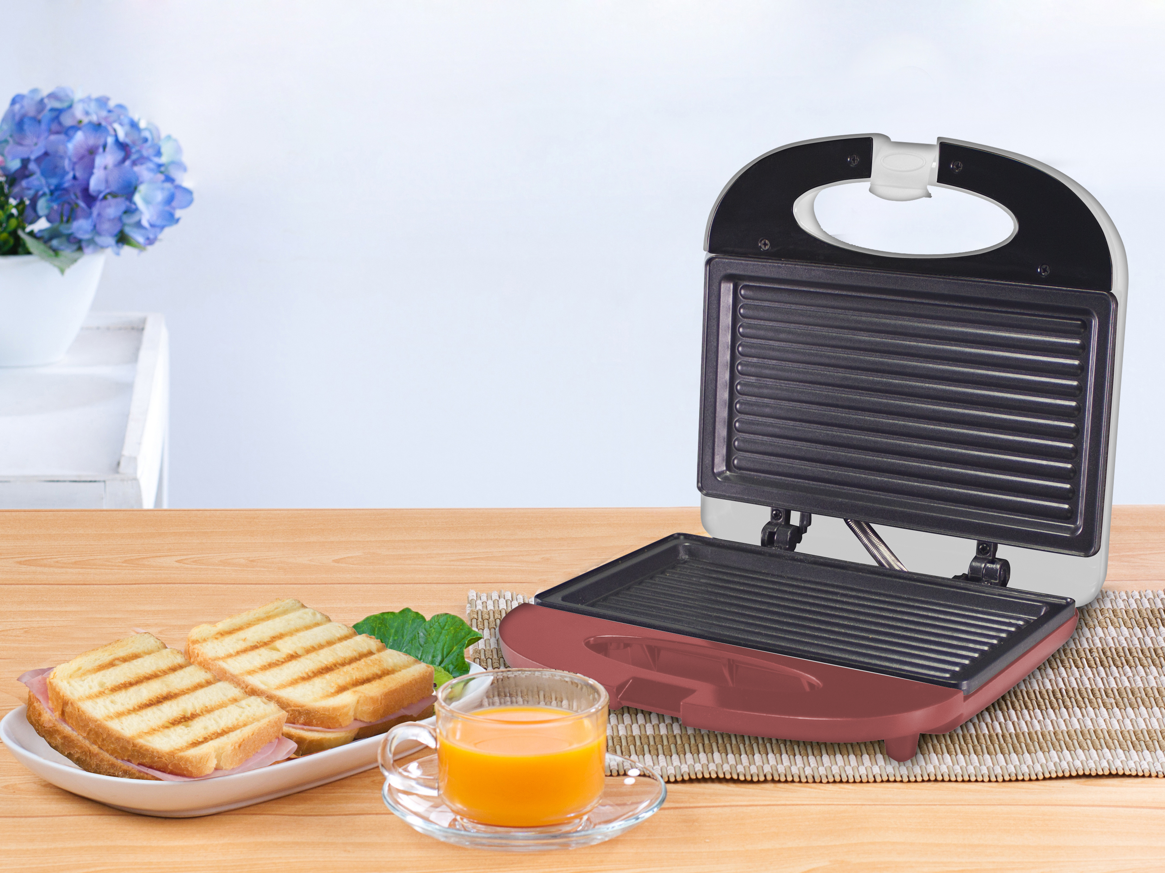 Una sandwichera con panini grigliati, succo e fiori su un tavolo di legno.
