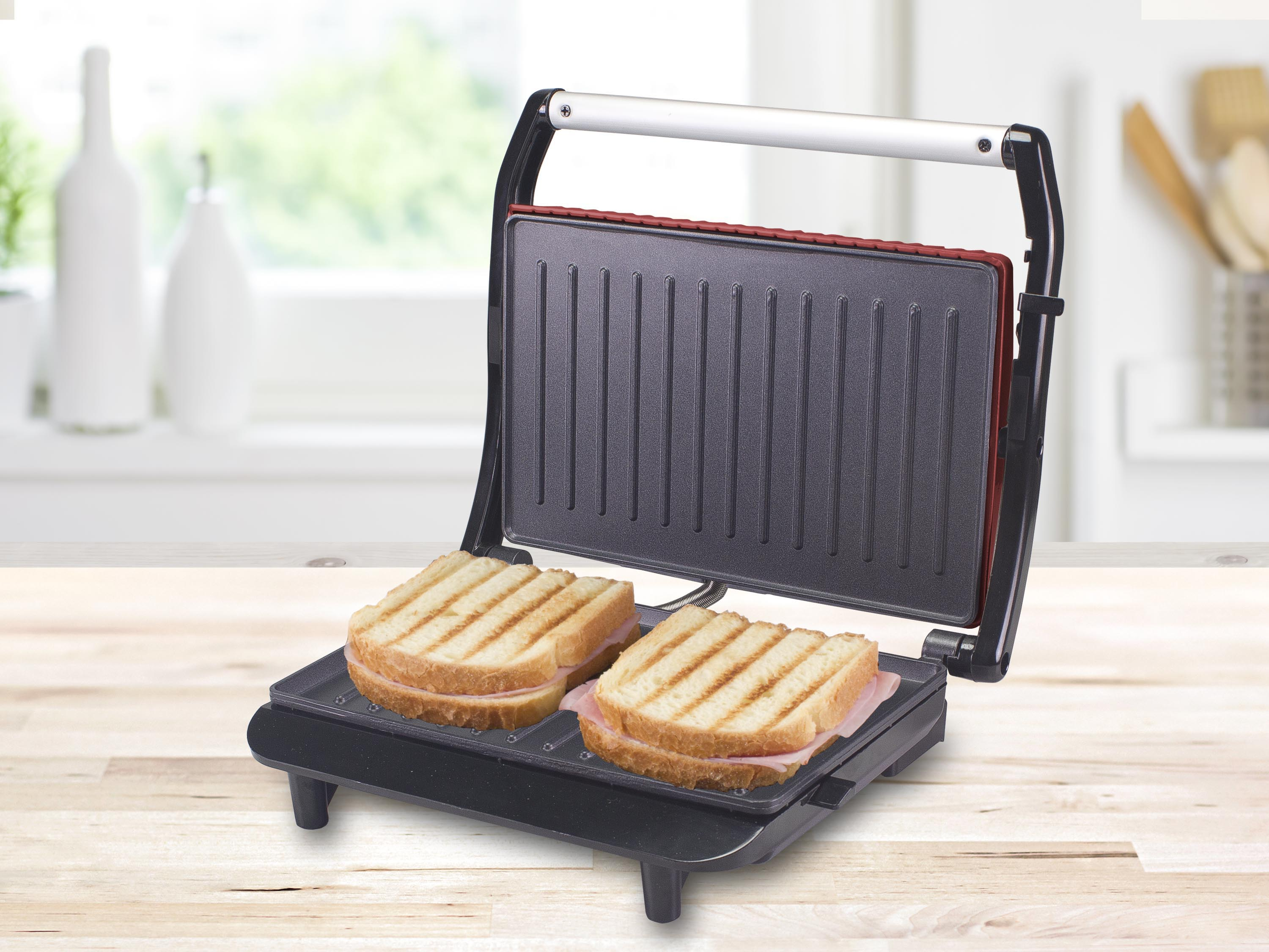 Pressa per panini aperta con due panini. Pane grigliato con prosciutto. Bottiglie bianche sullo sfondo.