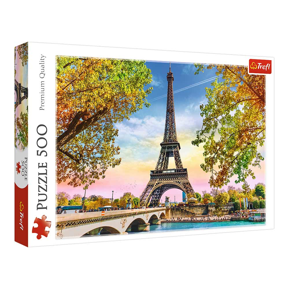 Une boîte de puzzle Trefl montre la tour Eiffel. Des arbres aux feuilles jaunes encadrent la tour. Un pont traverse l'eau devant.