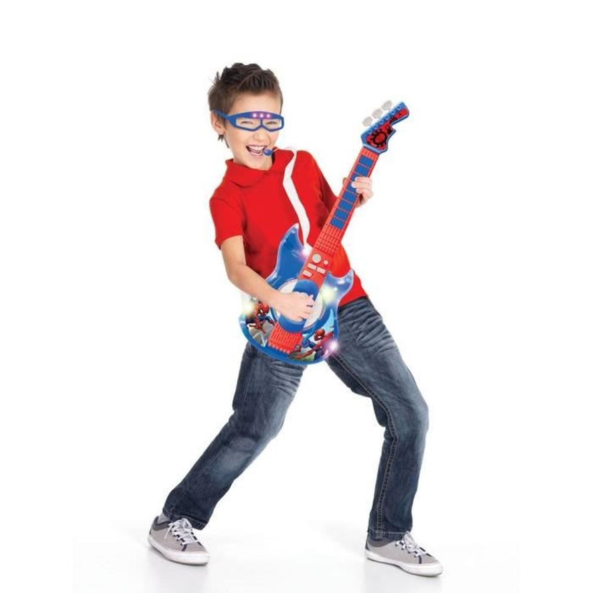 Un niño con gafas, camiseta roja y vaqueros toca una guitarra de juguete. La guitarra es azul y roja con gráficos de Spider-Man.