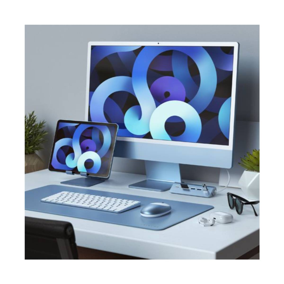 Ein moderner Schreibtisch mit blauem iMac, iPad, Tastatur, Maus und Zubehör. Blaue abstrakte Kunst wird auf Bildschirmen angezeigt.