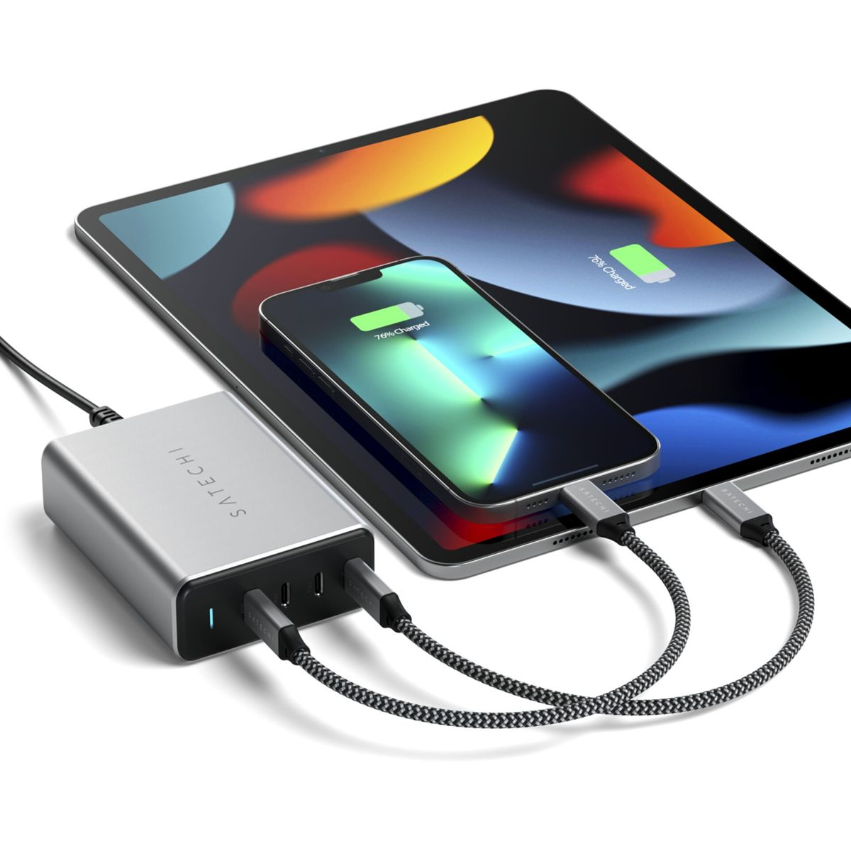 Cargador plateado con teléfono y tableta, ambos al 76% de carga. Los cables conectan los dispositivos al cargador. Fondo blanco.