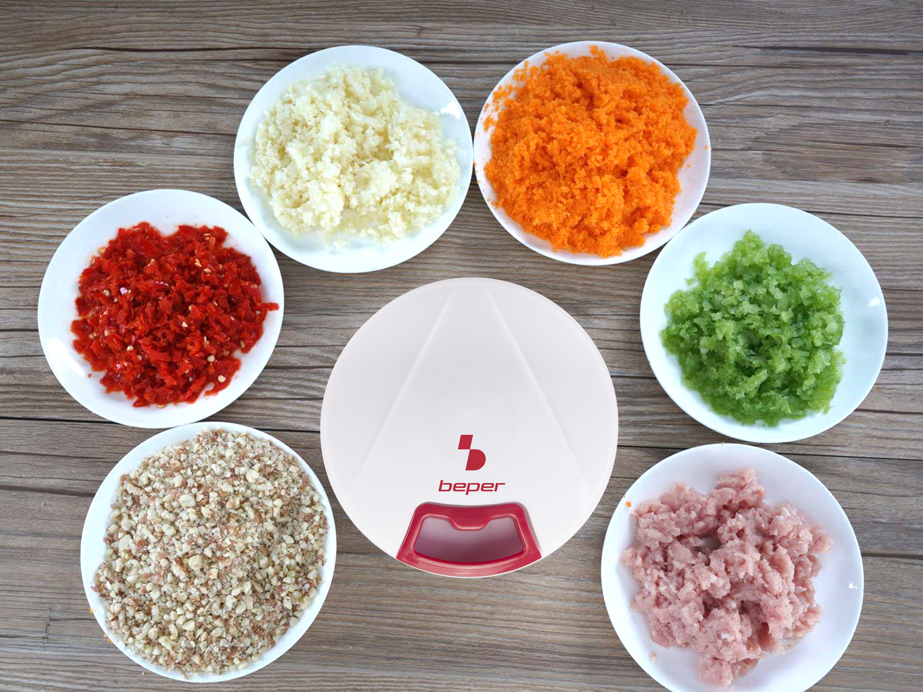 Un robot da cucina circondato da piatti di ingredienti tritati: aglio, carote, peperoni, sedano, noci e carne.