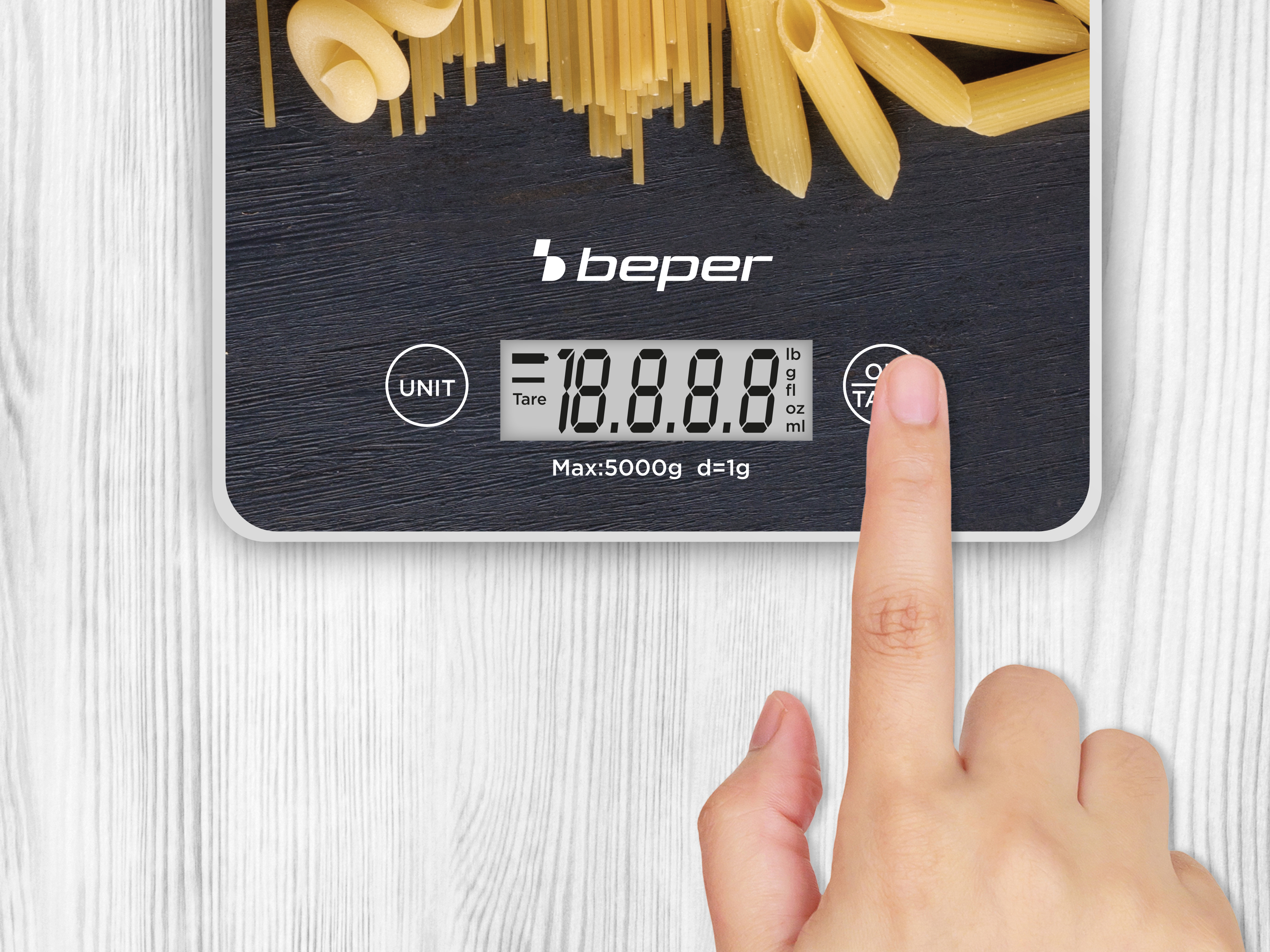 Una bilancia da cucina con pasta sopra. Un dito tocca il pulsante tara. Lo sfondo è in legno bianco.