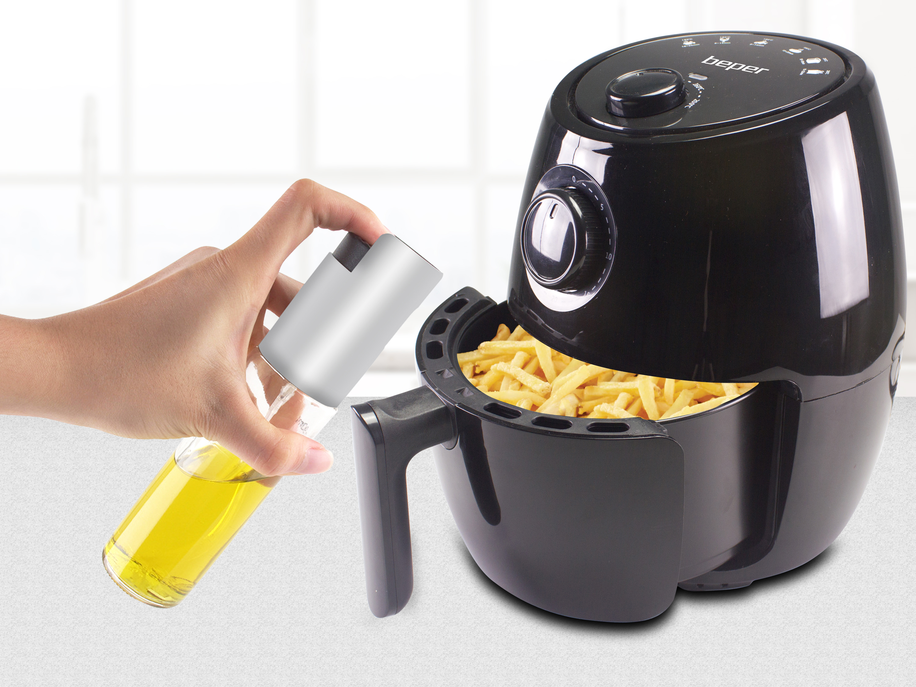 Mano che tiene una bottiglia d'olio, friggitrice ad aria con patatine fritte. Friggitrice nera, mano con bottiglia, olio giallo, patatine fritte dentro.