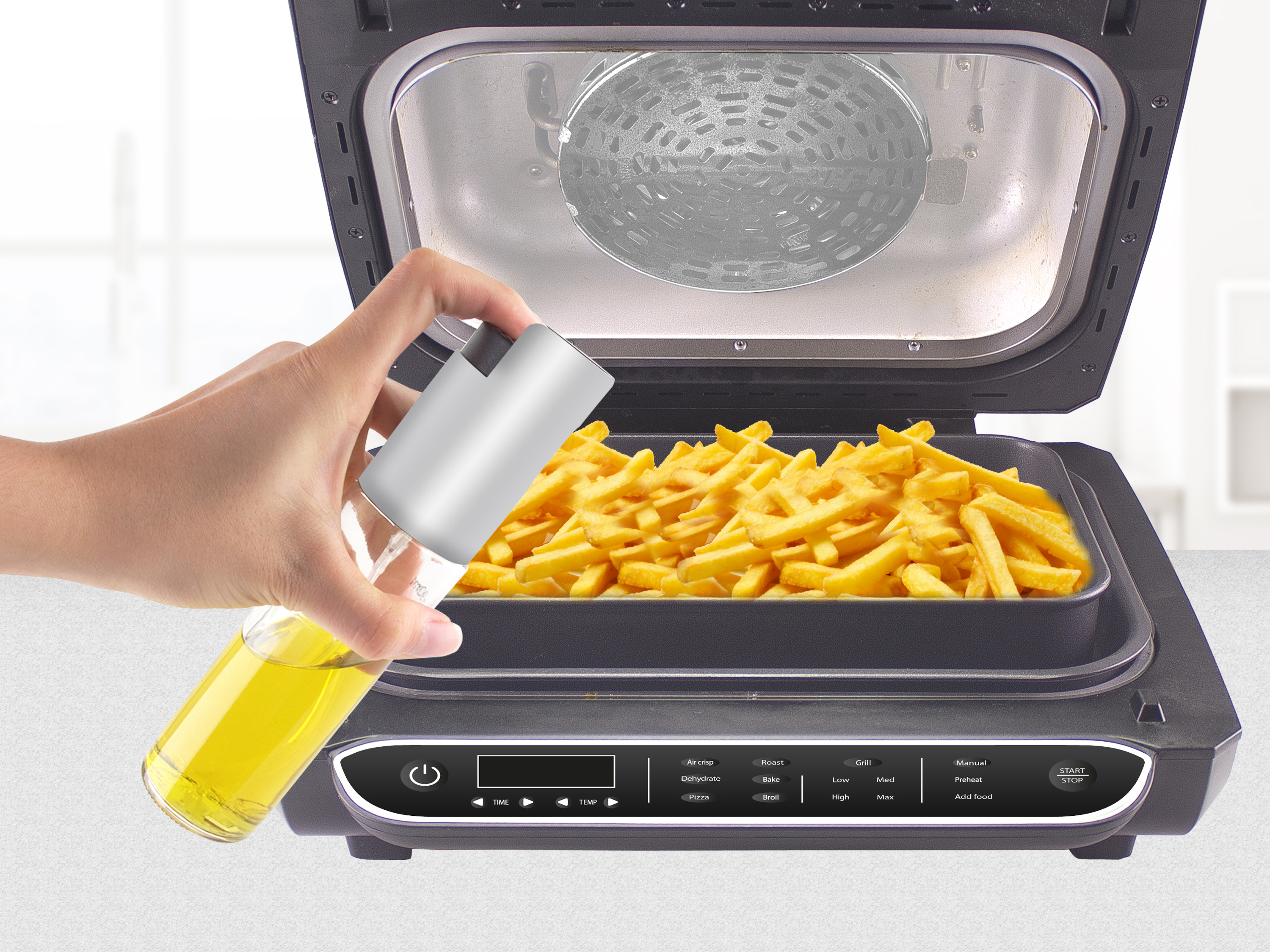 Mano che spruzza olio su patatine fritte in una friggitrice ad aria. La friggitrice è aperta, con patatine fritte all'interno.