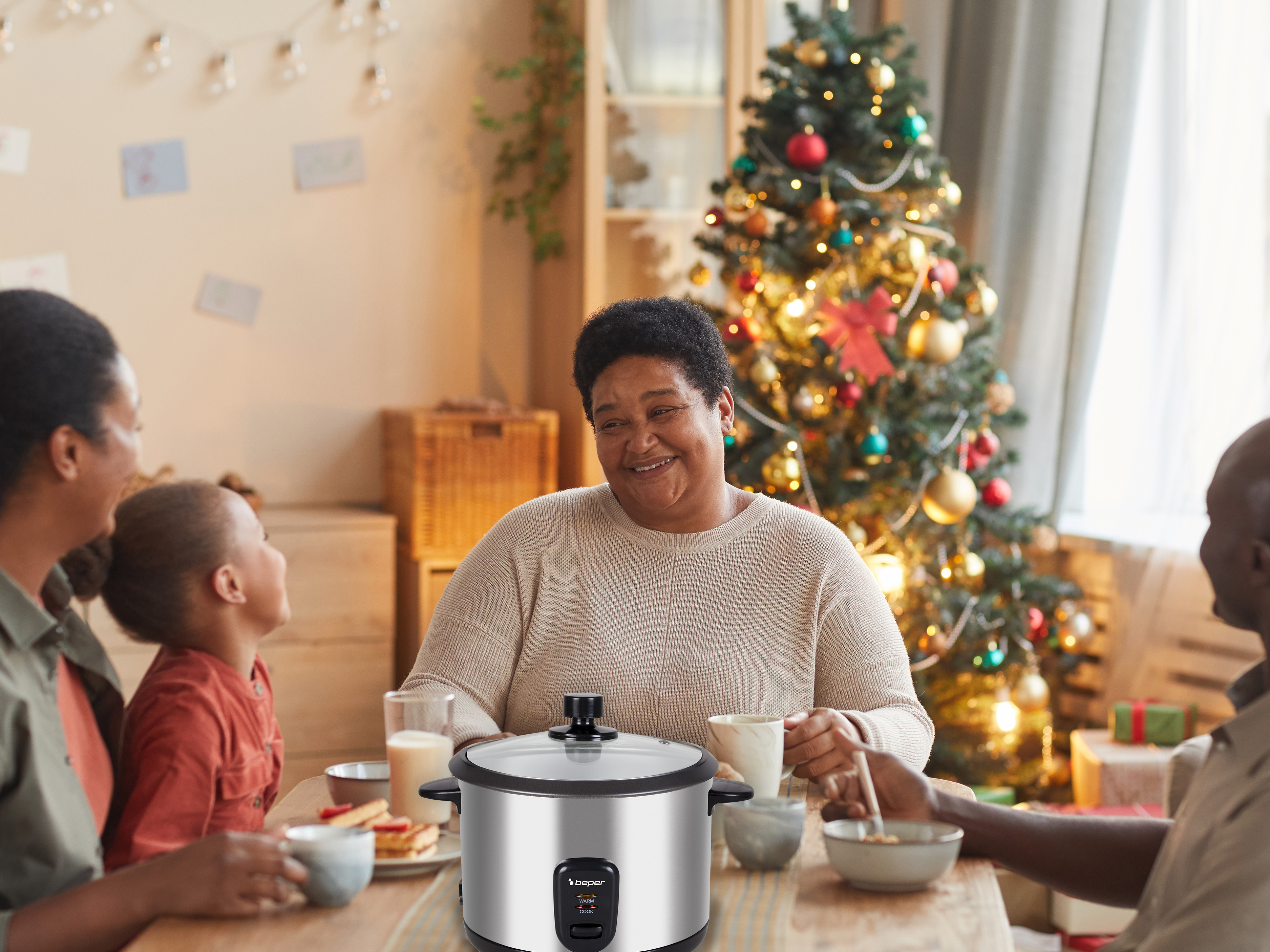 Famiglia a tavola con cuociriso. Albero di Natale sullo sfondo. Donna sorridente con una tazza.