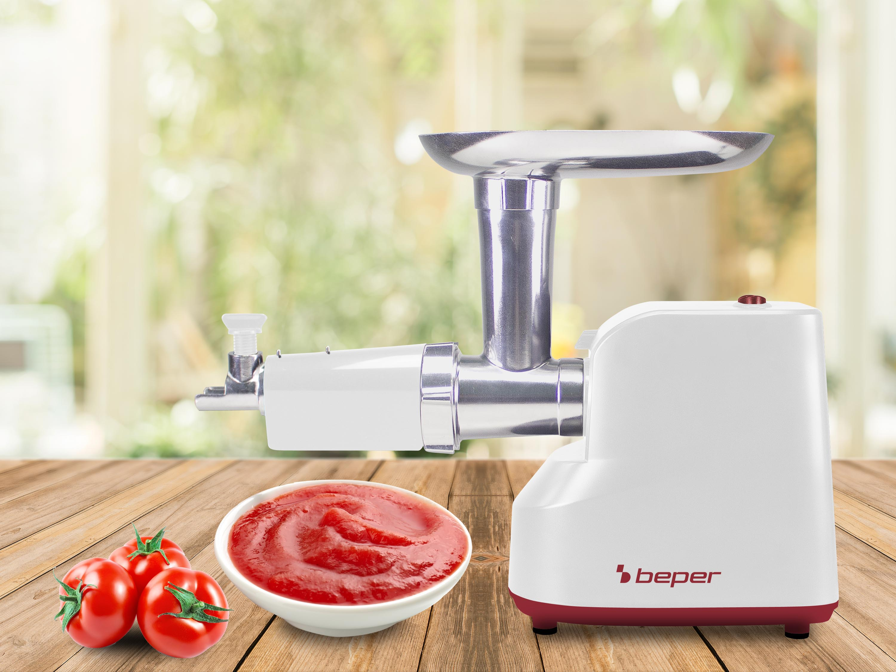 Ein weißer und silberner Fleischwolf mit Tomaten und Tomatensauce auf einem Holztisch.