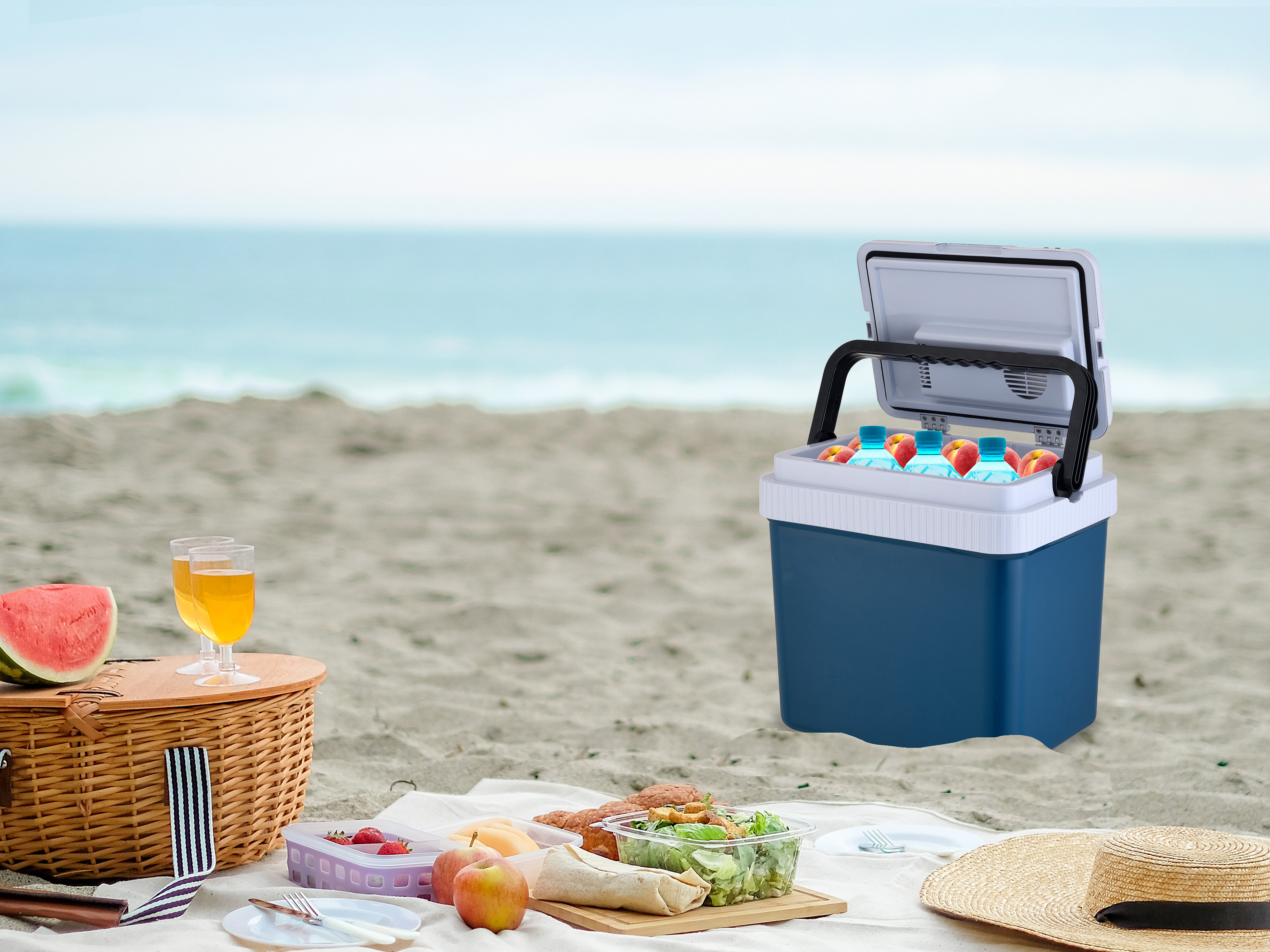 Picnic sulla spiaggia con cibo, bevande, ghiacciaia e cappello da spiaggia. Lo sfondo è l'oceano.