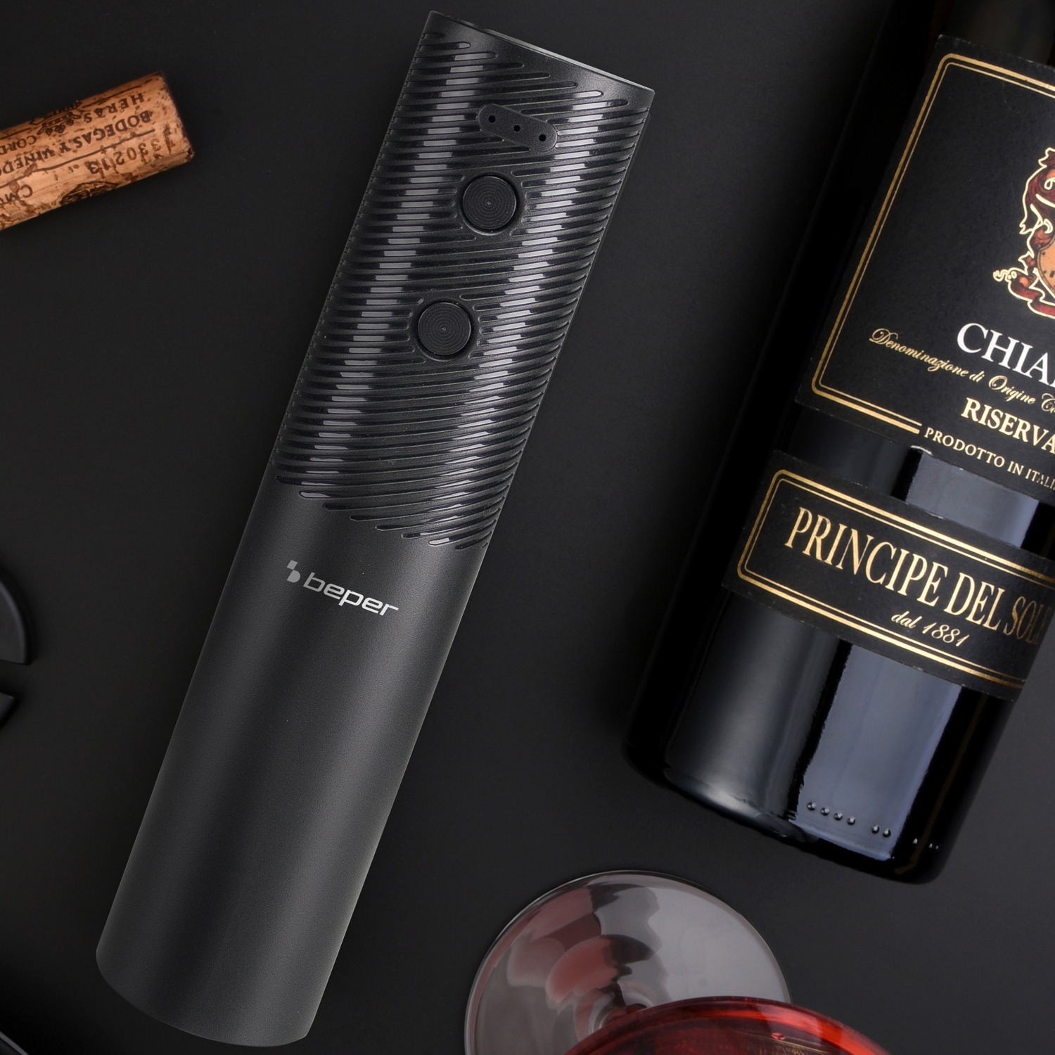 Un cavatappi elettrico nero e una bottiglia di vino. Un tappo e un bicchiere da vino sono visibili su una superficie nera.