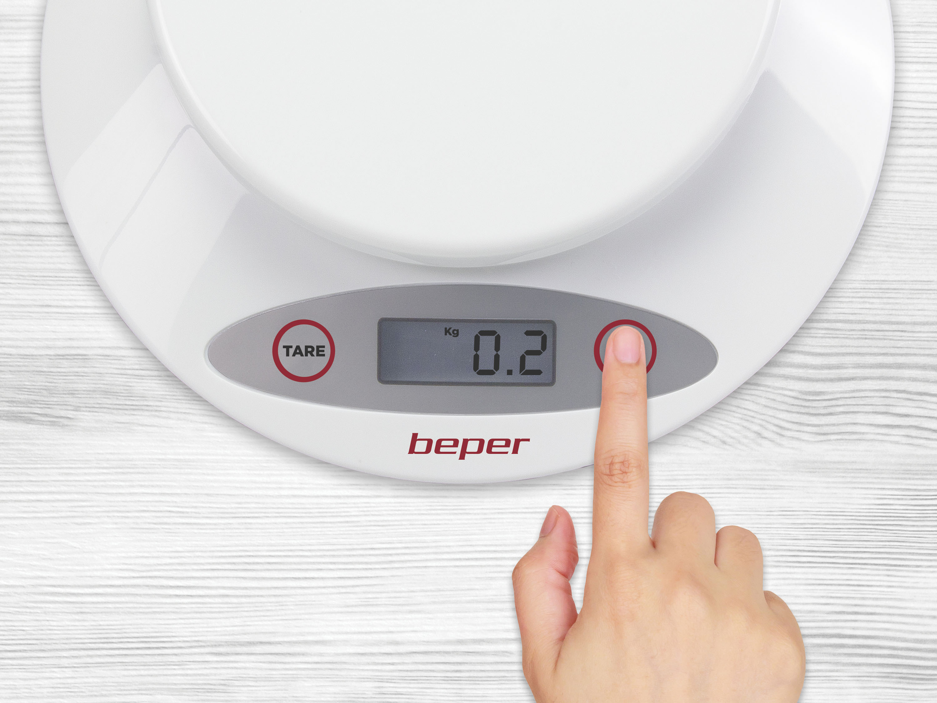Una mano preme un pulsante rosso su una bilancia da cucina bianca. Il display mostra 0,2 kg. La bilancia è su legno.