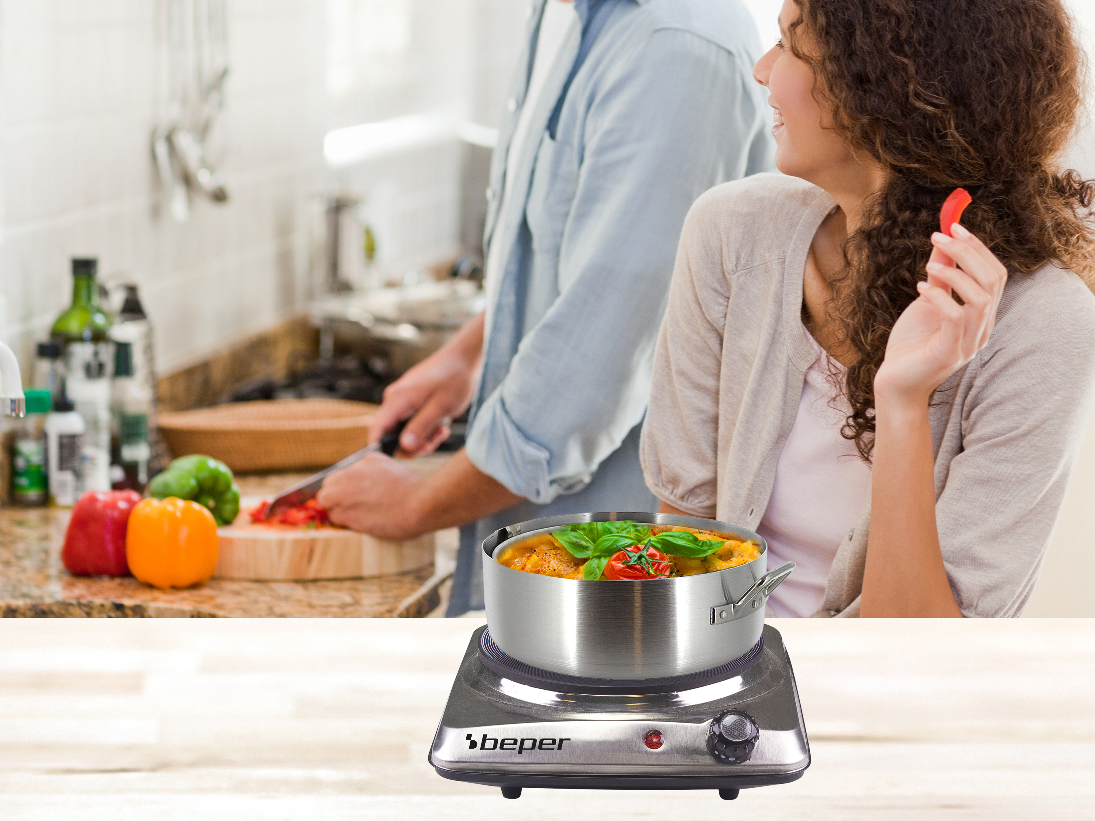 Una coppia in cucina, uno taglia verdure, l'altro tiene un pezzo di peperone rosso.