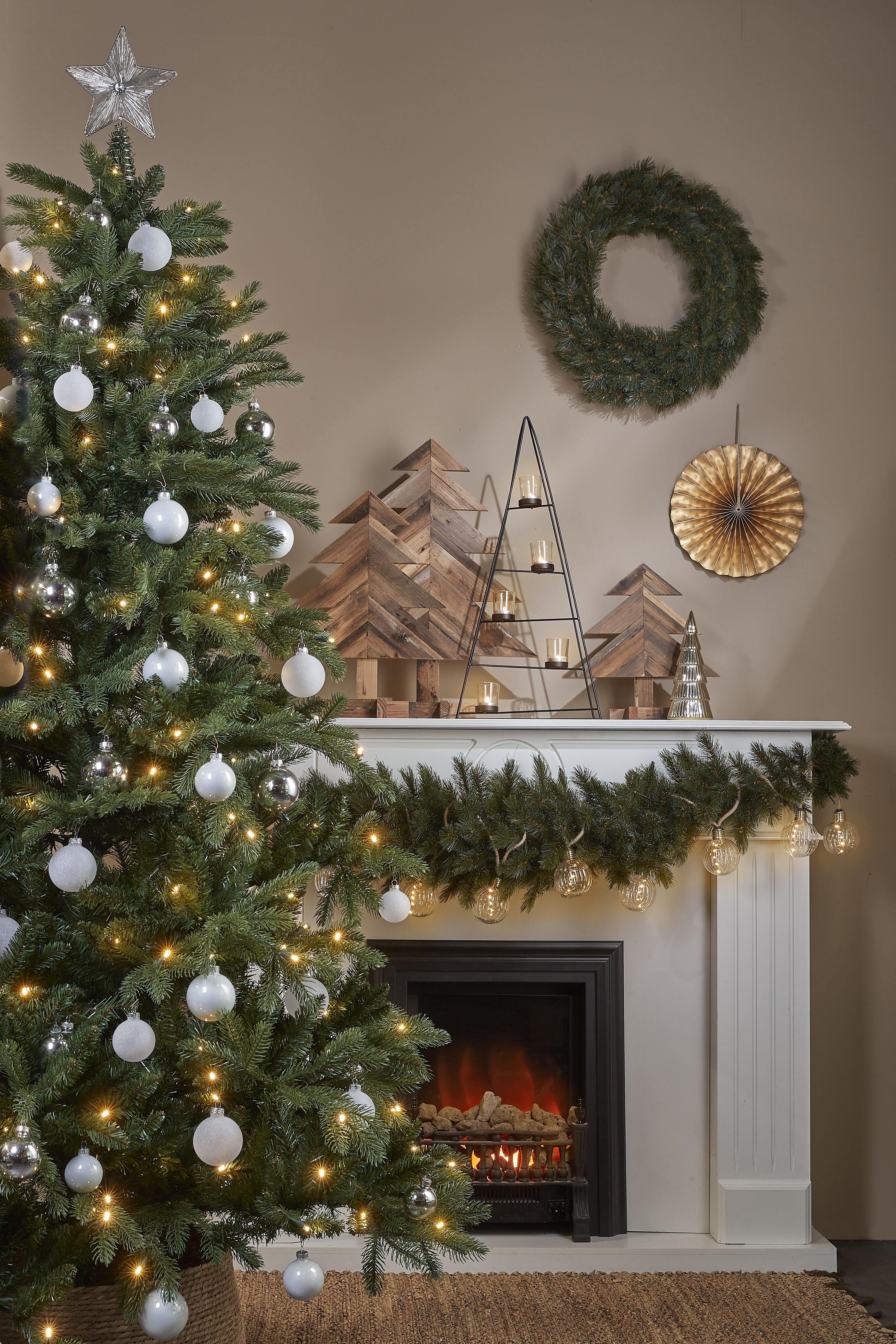 Scène de Noël avec sapin, cheminée, ornements et décorations. Le sapin est décoré d'ornements blancs et argentés.