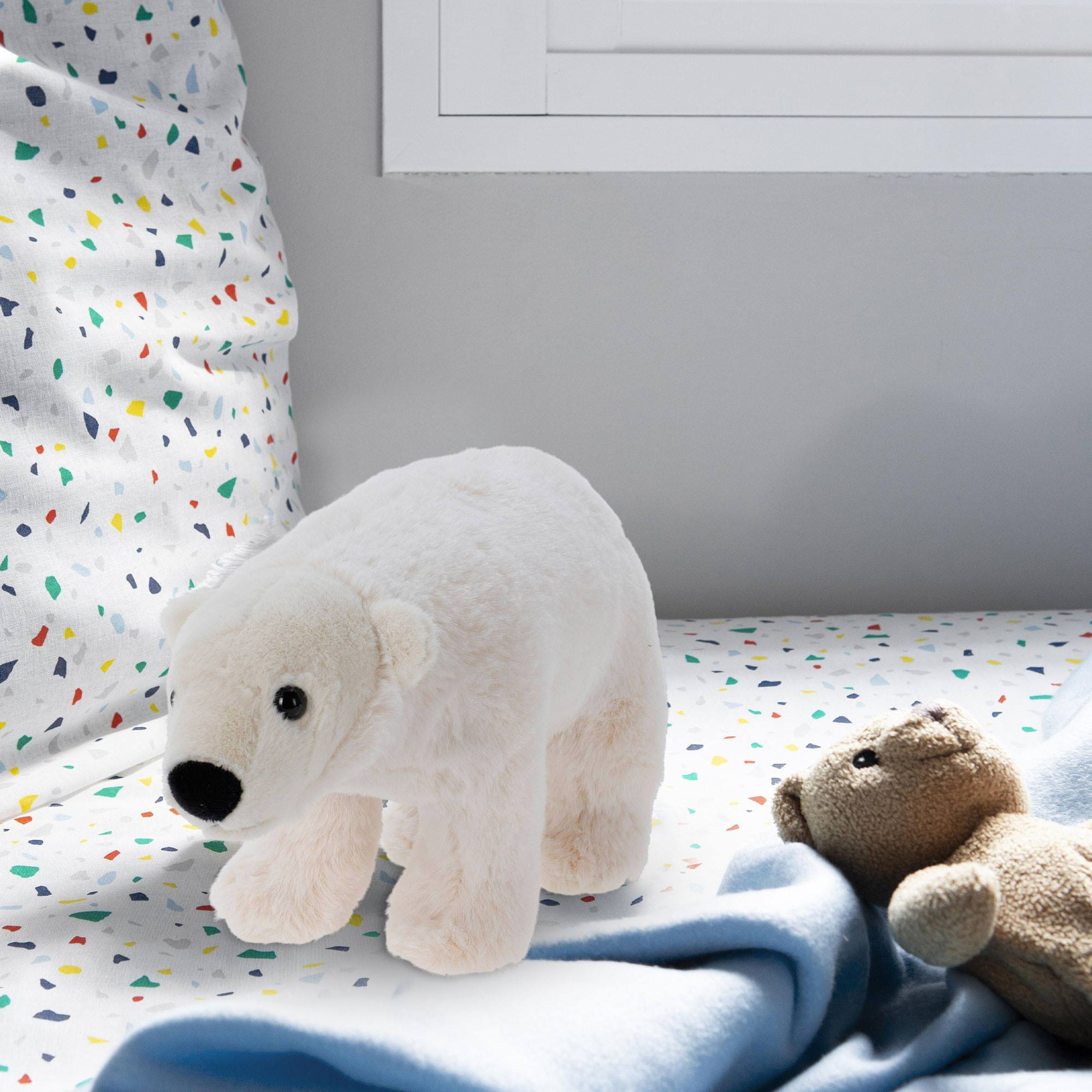 Un oso polar blanco y un osito de peluche marrón están en una cama con una sábana colorida y una manta azul.