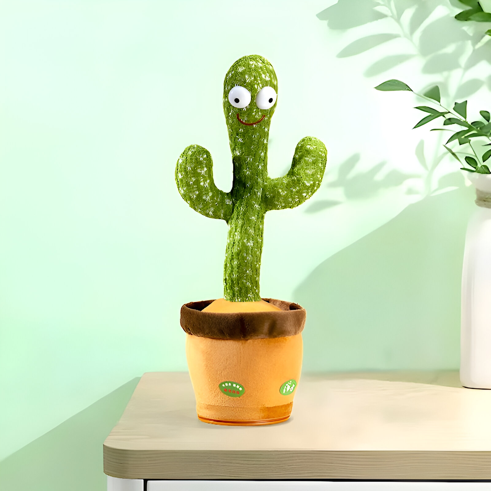 Un juguete de cactus verde con ojos y boca sonriente en una maceta naranja sobre una mesa.