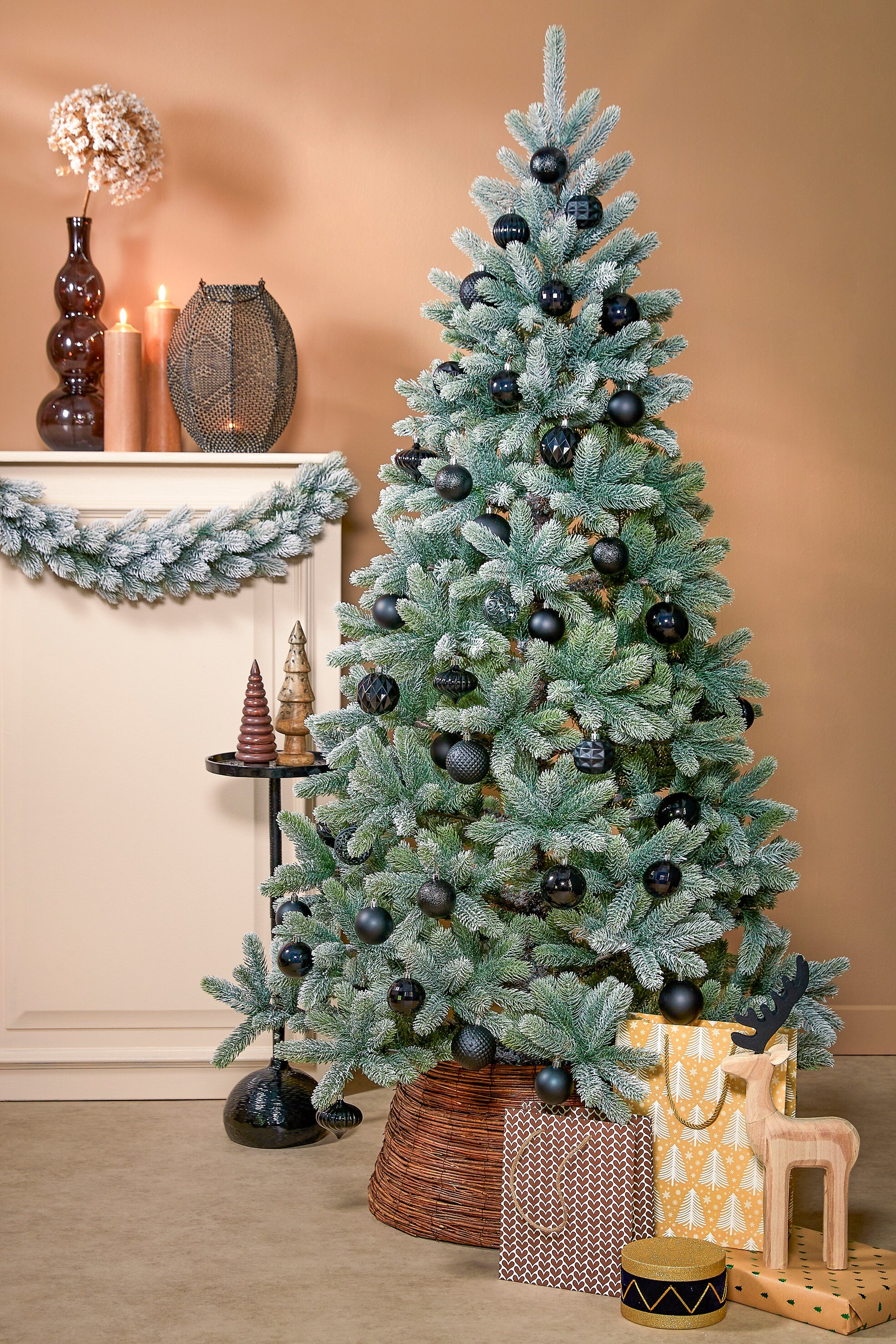 Un arbre de Noël décoré avec des ornements noirs. Des cadeaux et des décorations l'entourent. Le fond est un mur beige.